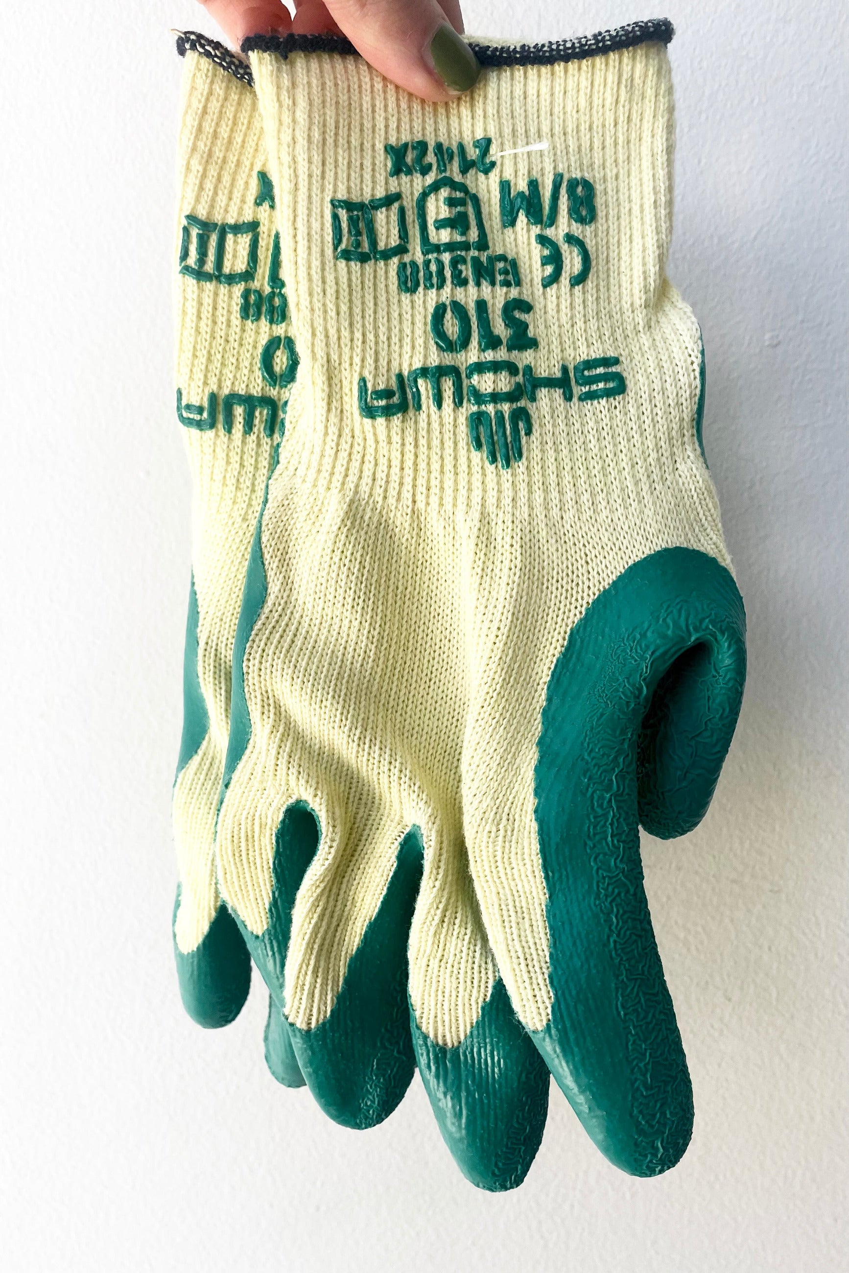 A hand holds the pair of Atlas Super Grip Gloves Medium against white backdrop ©Sprout Home