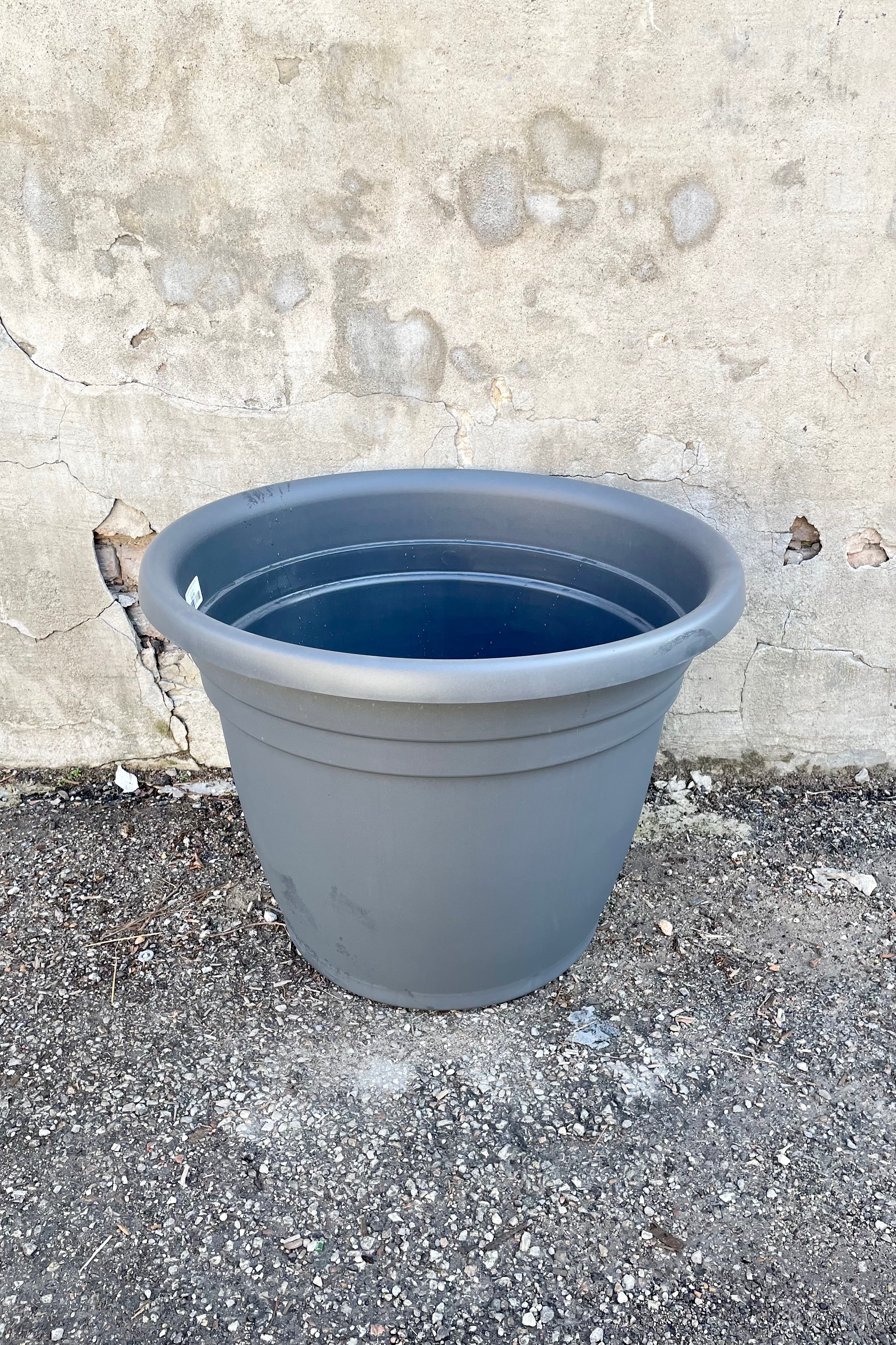 The emma round charcoal 25" planter against a concrete wall.