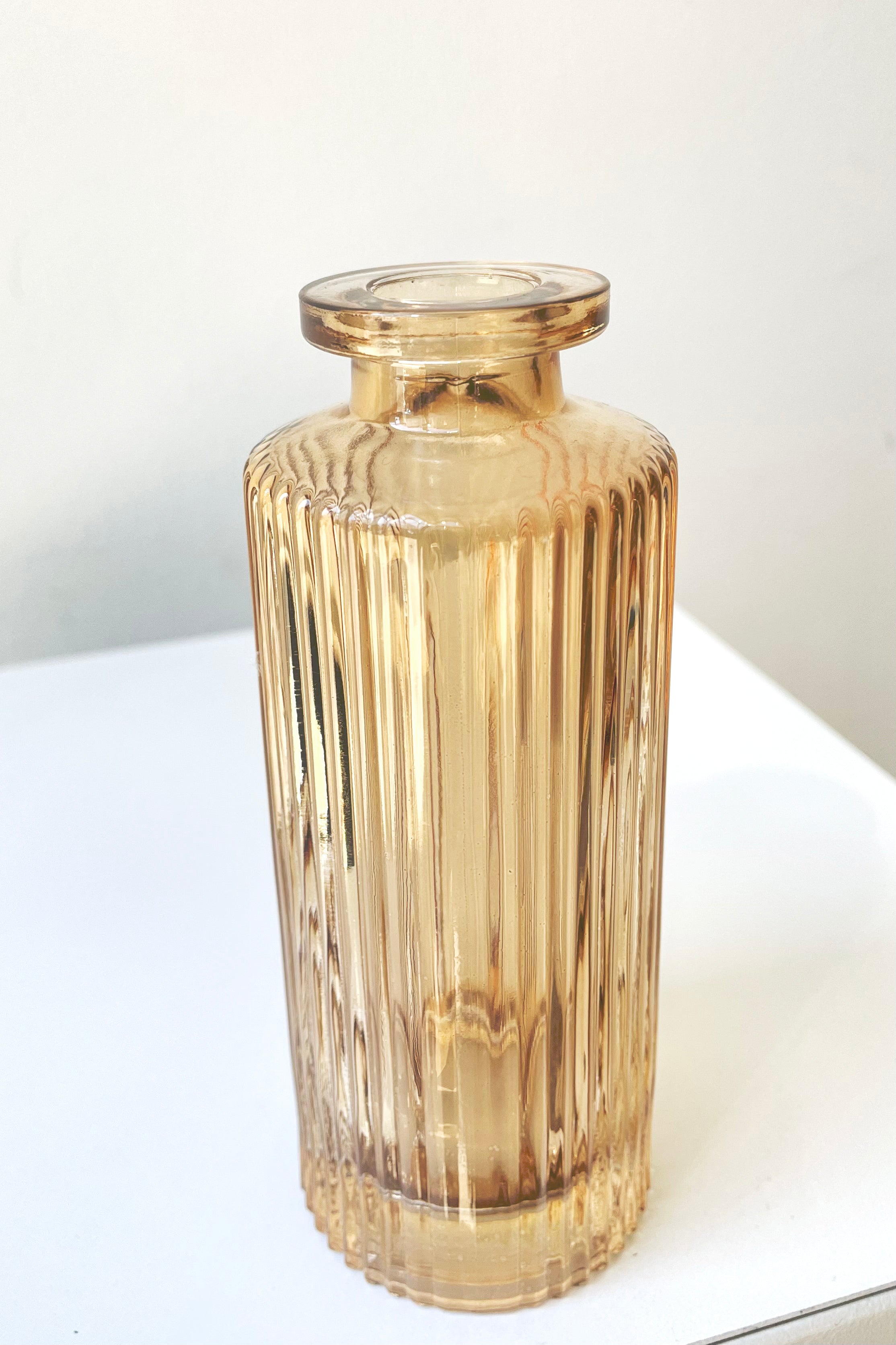 A slight overhead view of the Amber Pleated Glass Bottle Bud Vase against a white backdrop