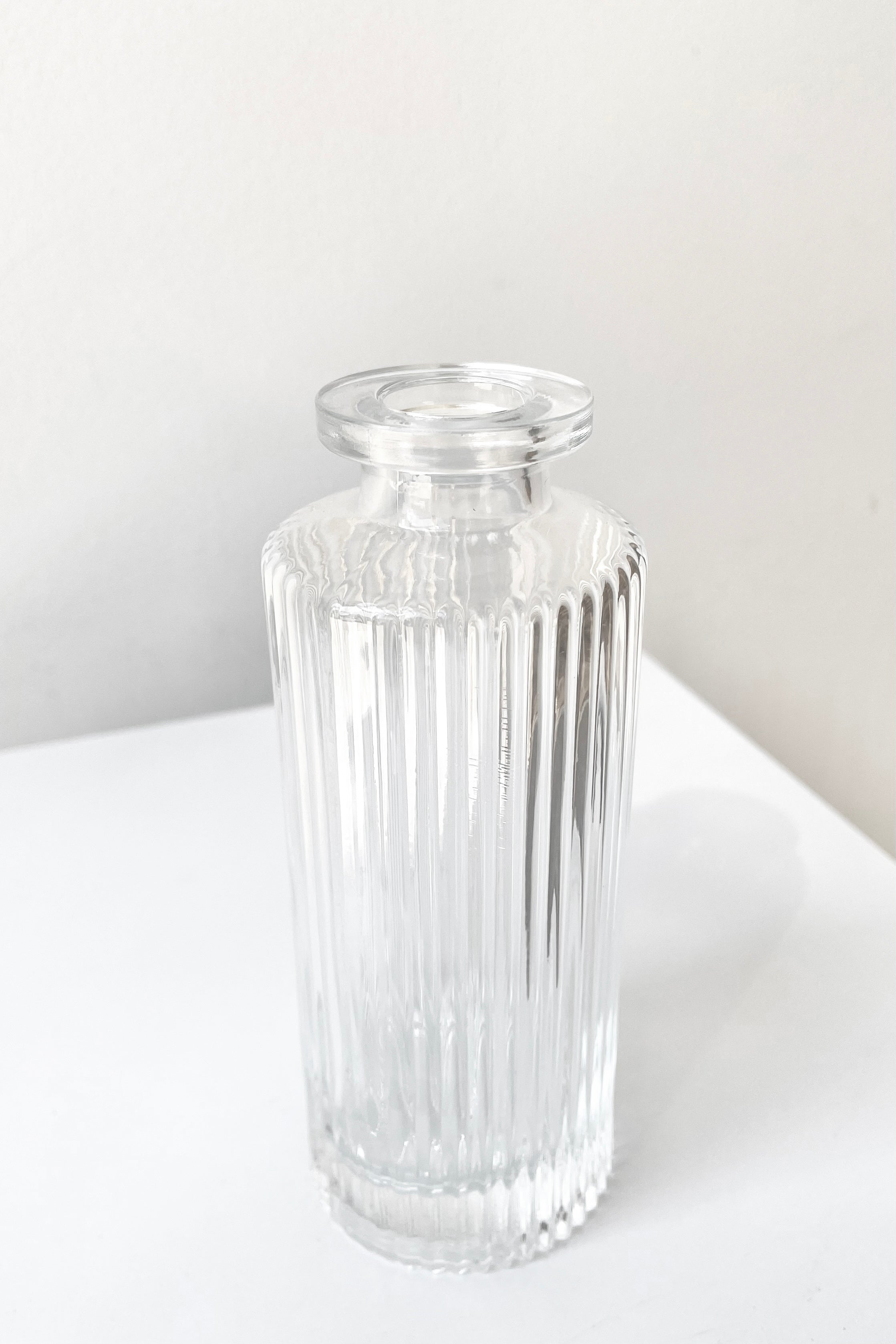 A slight overhead view of the Pleated Medicine Bud Vase in Clear against a white backdrop