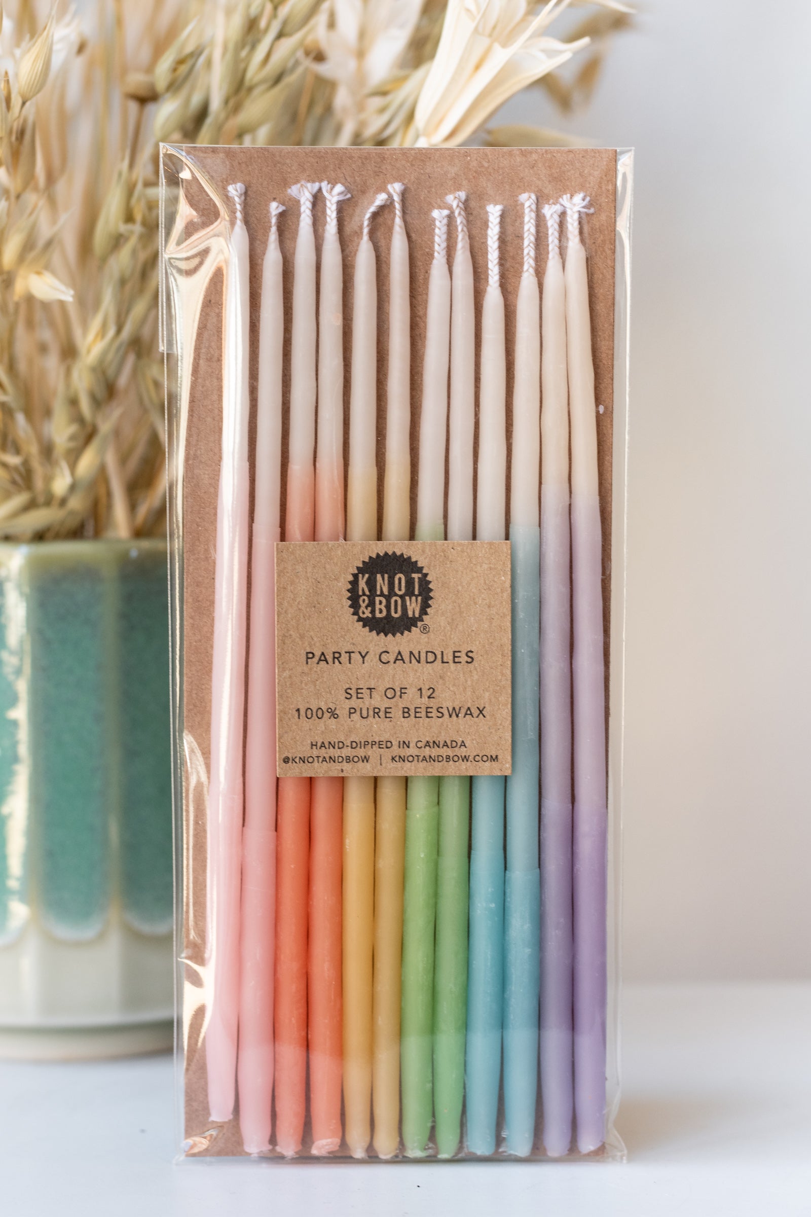 Tall ombre assorted beeswax birthday party candles by knot and bow in front of natural dried floral arrangement