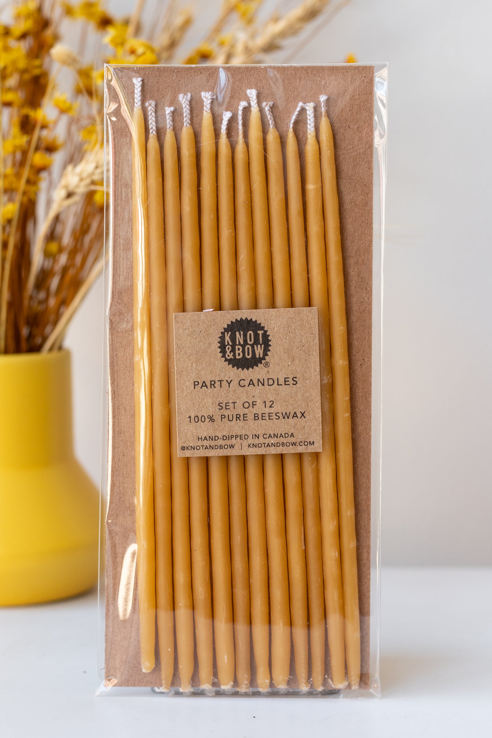 Natural tall beeswax birthday party candles by knot and bow in front of yellow dried floral arrangement