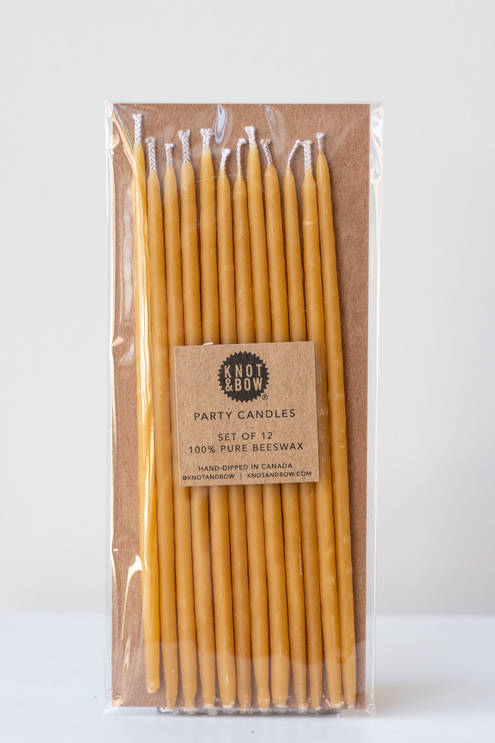 Natural tall beeswax birthday party candles by knot and bow in front of white background