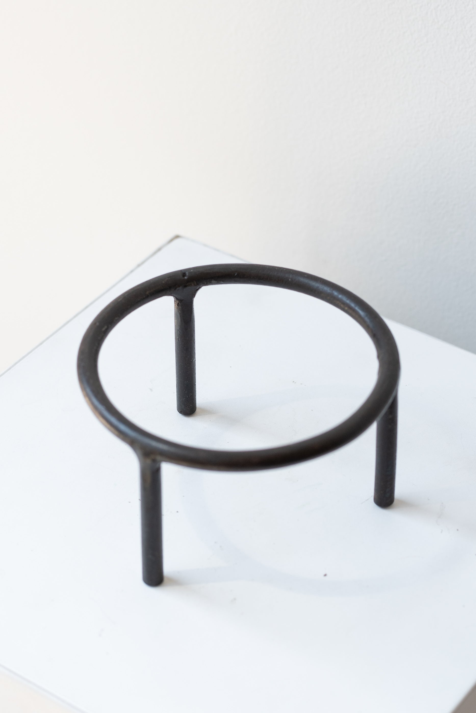 4 inch iron metal tripod pot stand on a white surface in a white room