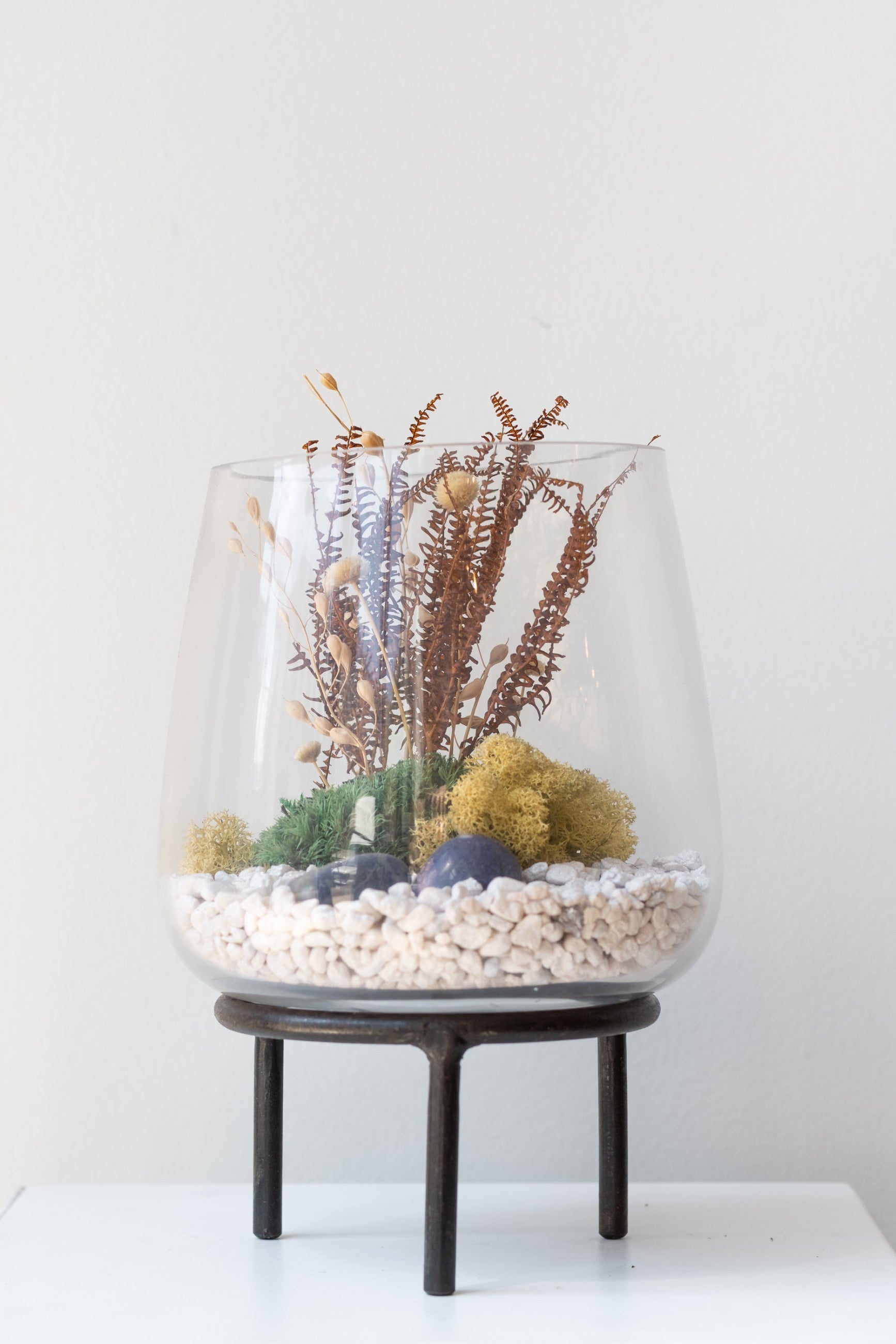 Glass terrarium on top of 4 inch iron metal tripod pot stand on a white surface in a white room ©Sprout Home
