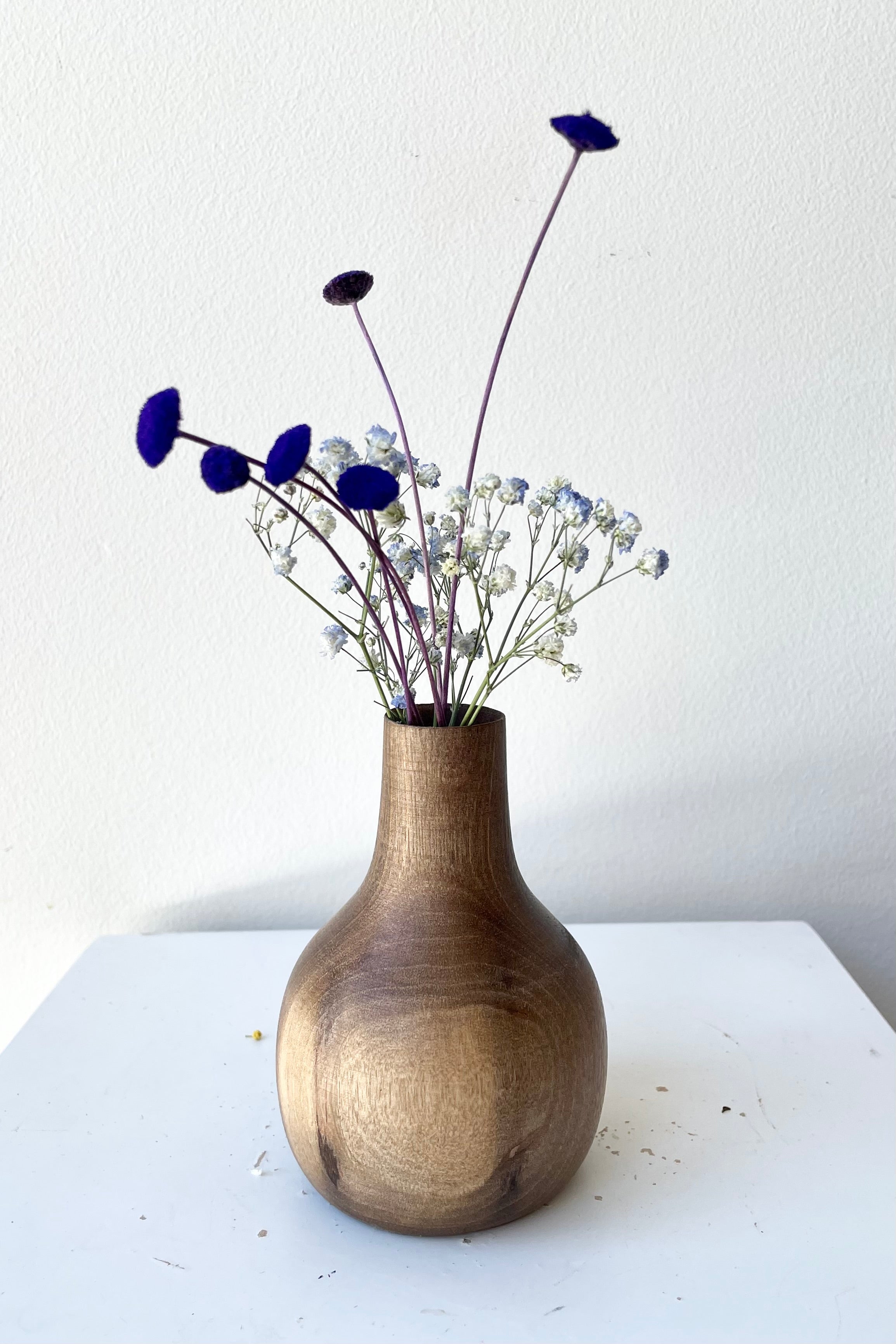 The Nina walnut wood vase against a white wall with dried floral at Sprout Home.
