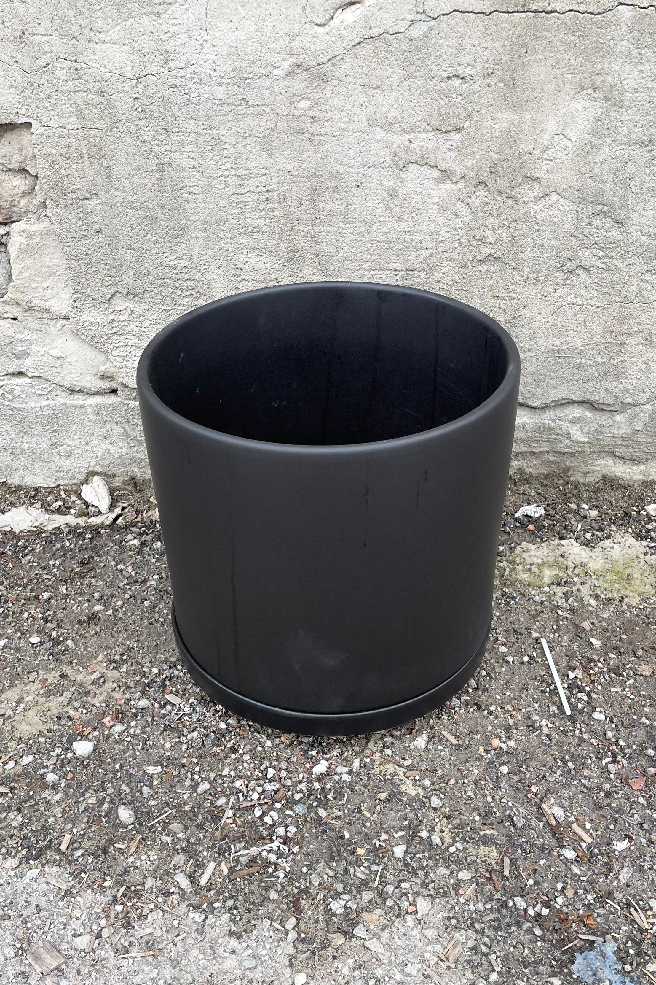 The 10" solid cylinder and saucer in black against a concrete wall.