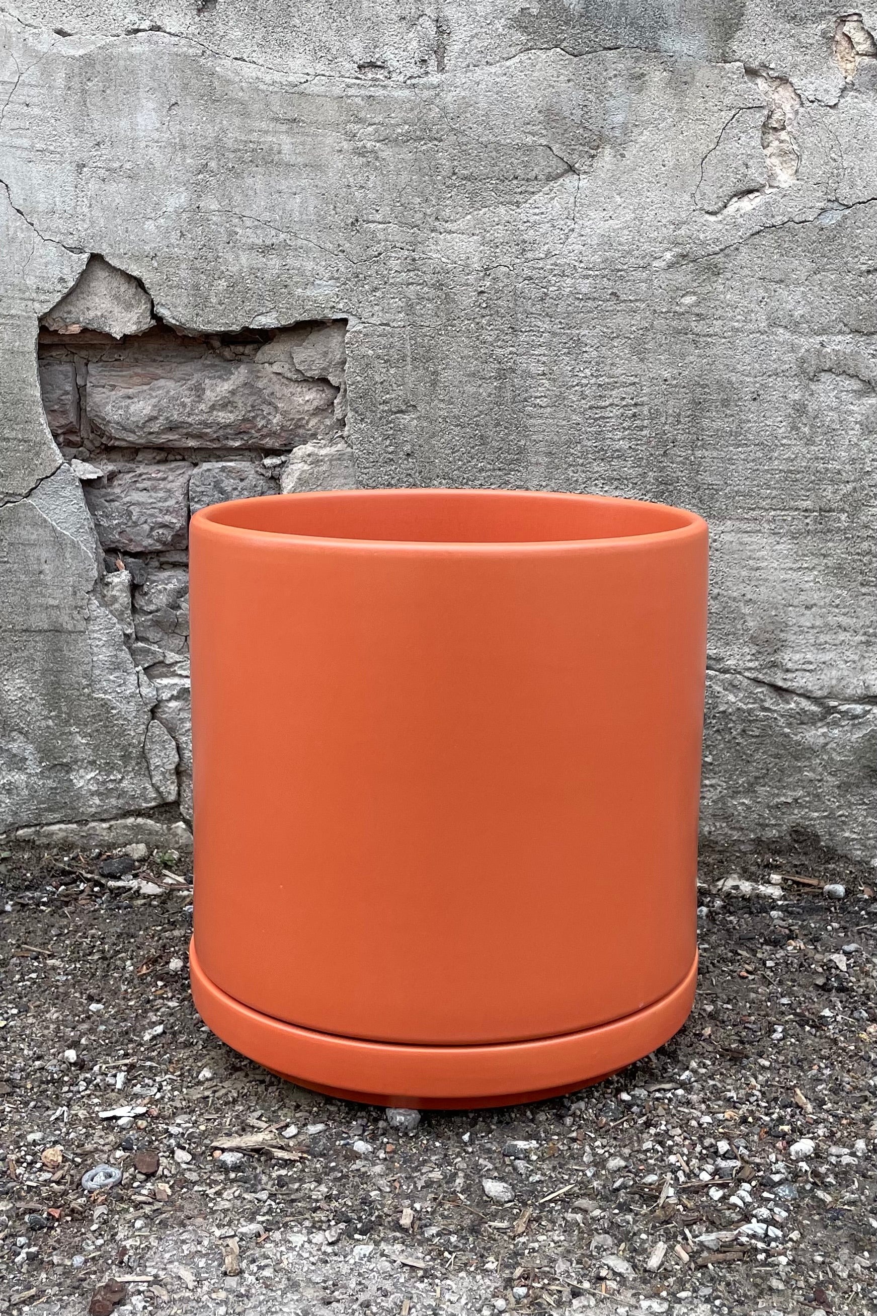 10" rust solid cylinder and saucer against a cement wall.