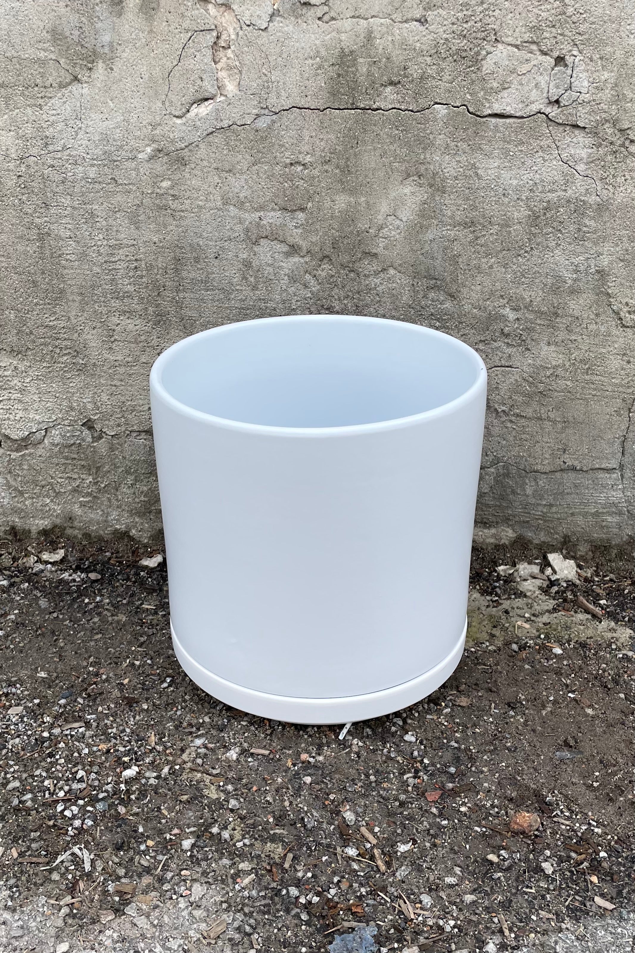 The 10" solid cylinder and saucer in white against a cement wall.