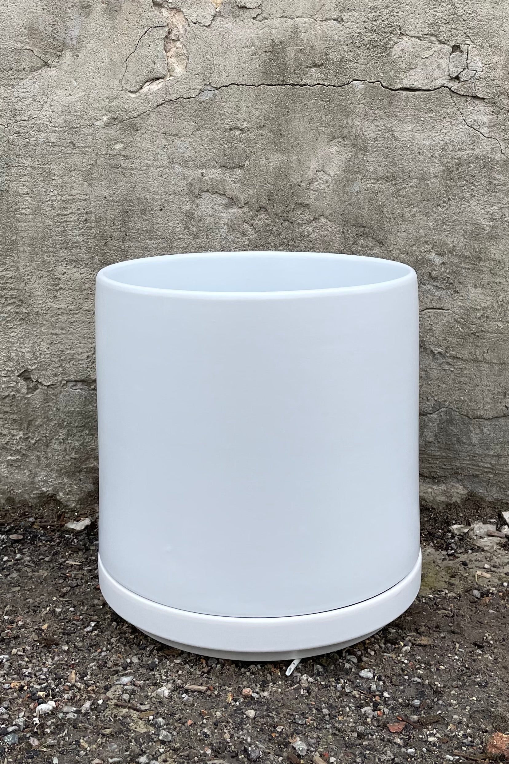 The 10" solid cylinder and saucer in white against a cement wall.