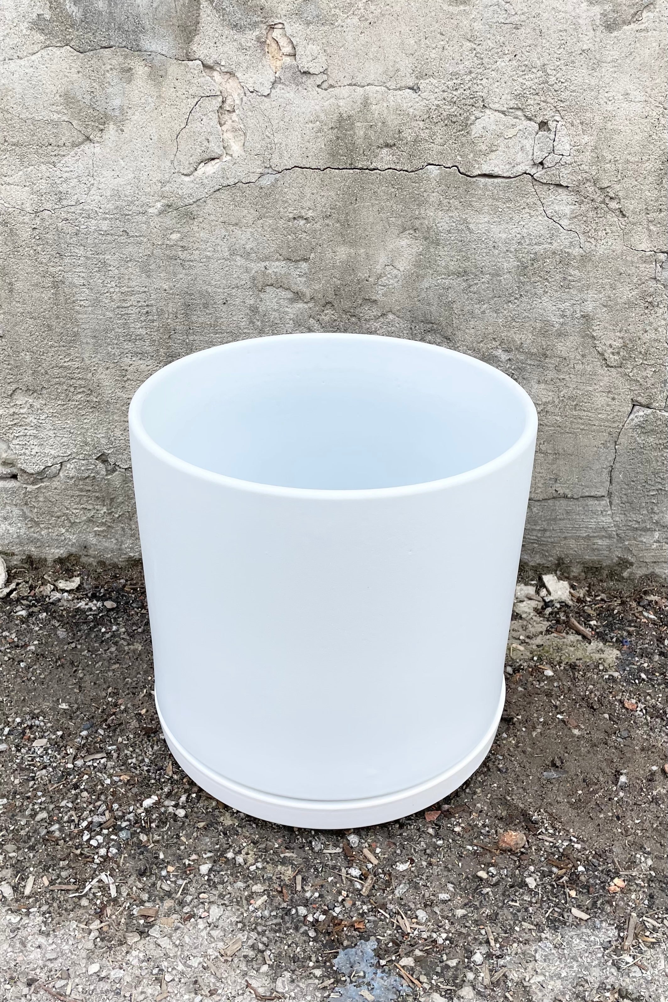 The 12" solid cylinder and saucer in white against a cement wall.