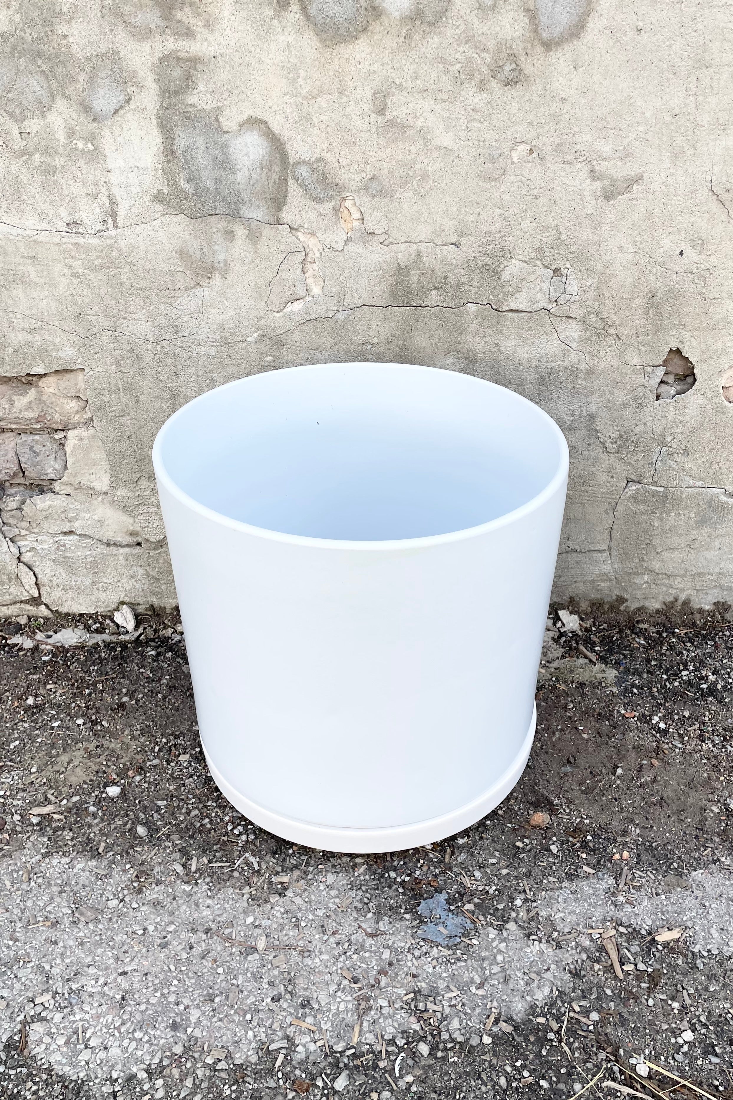 15" white solid cylinder and saucer against a cement wall.