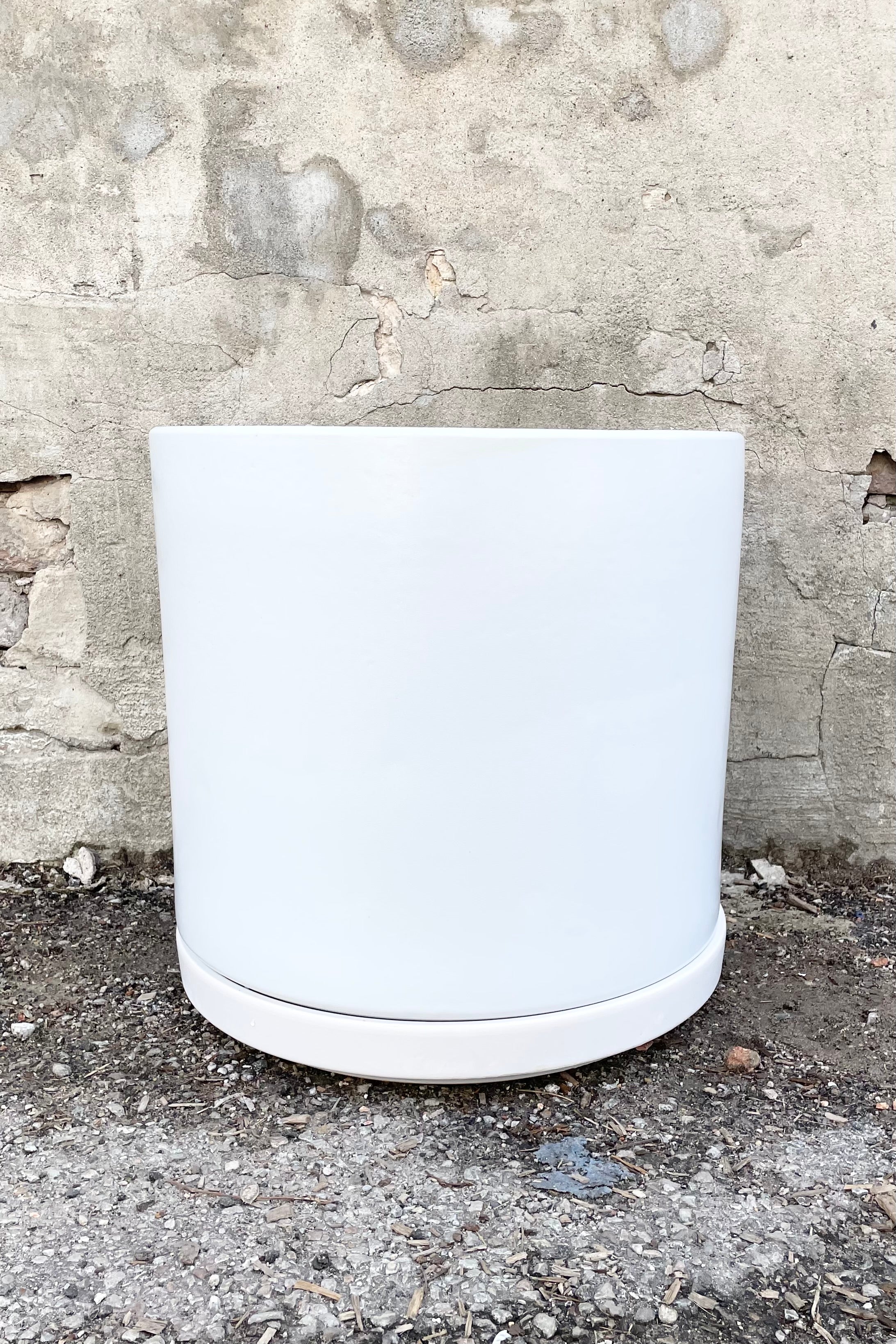 15" white solid cylinder and saucer against a cement wall.