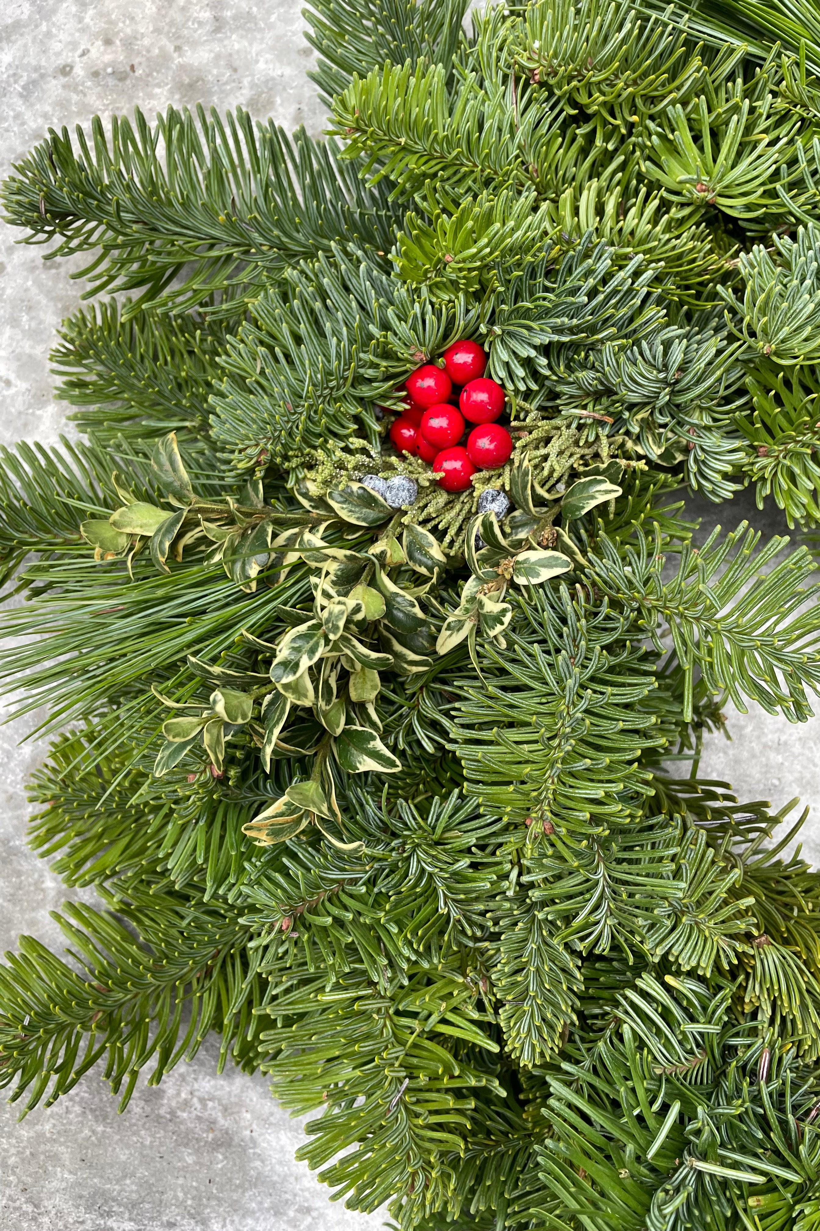 Detail of an evergreen wreath with pops of faux camellia berry and pine.