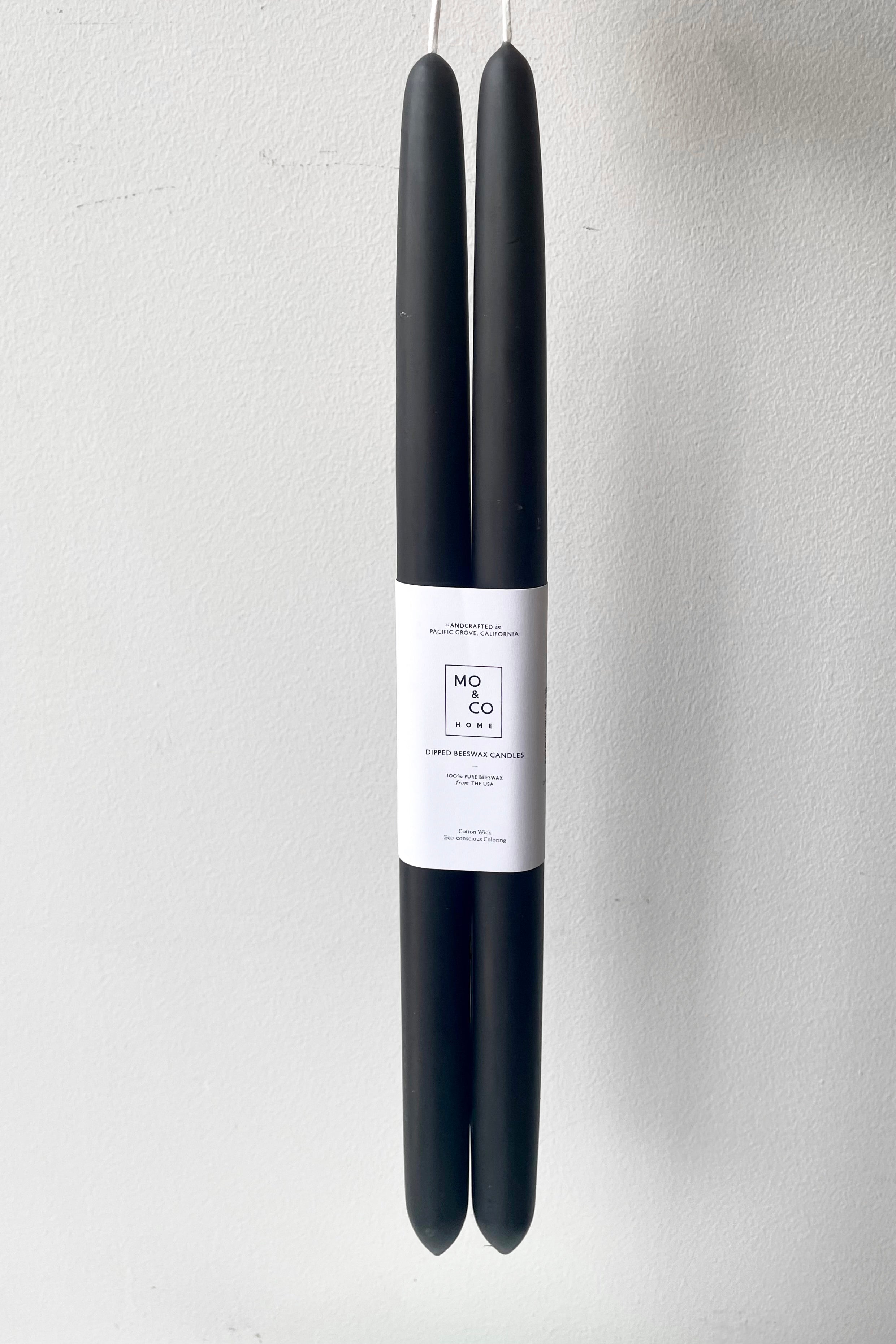 A hand holds the Charcoal 14" Taper Candles, pair against a white backdrop