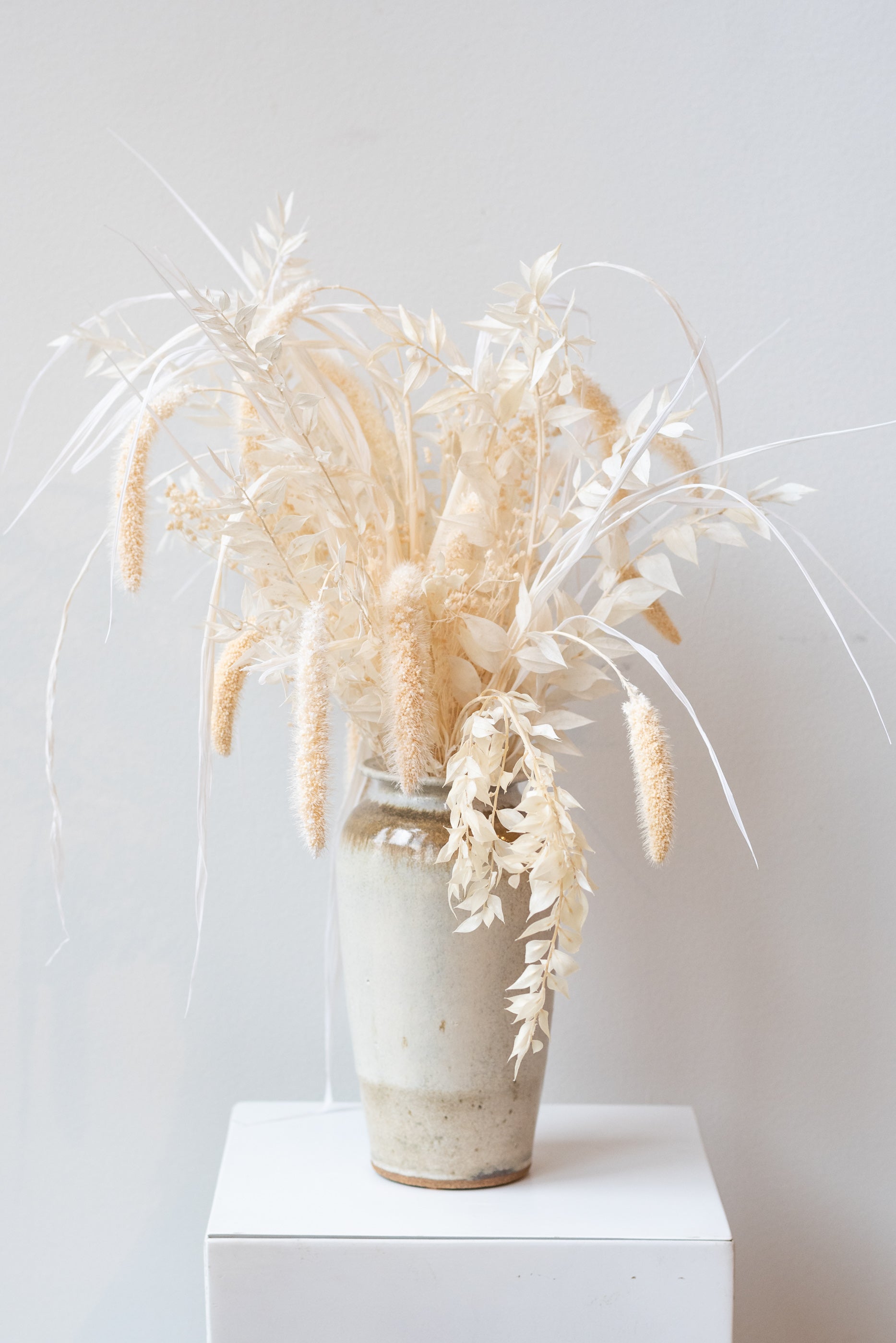 Bruning Pottery ivory and iron glazed tall ceramic vase in front of white background. Inside the vase is a bouquet of bleached preserved florals