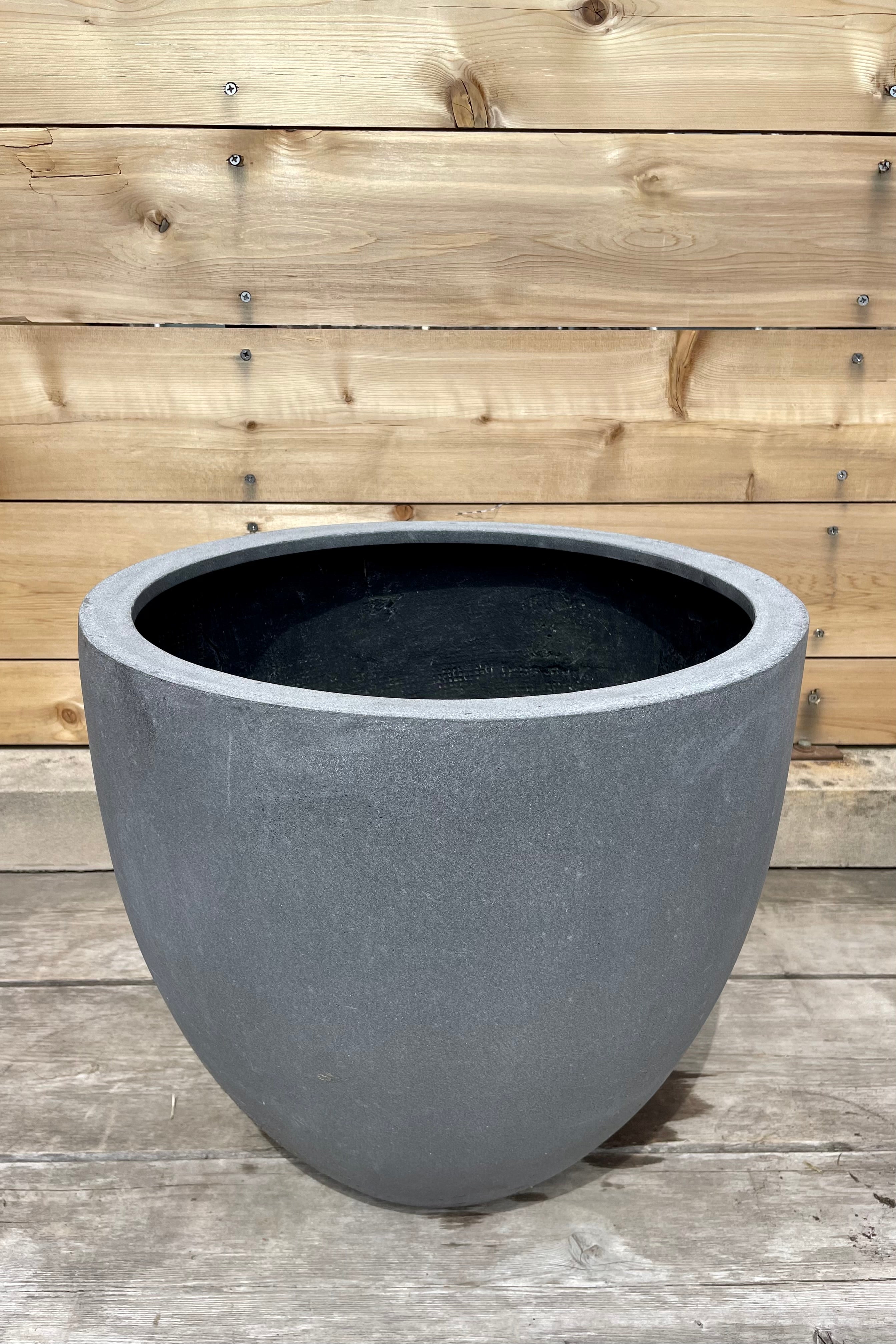 Detail of Jesslyn Pot Fiberstone grey medium against a wooden fence