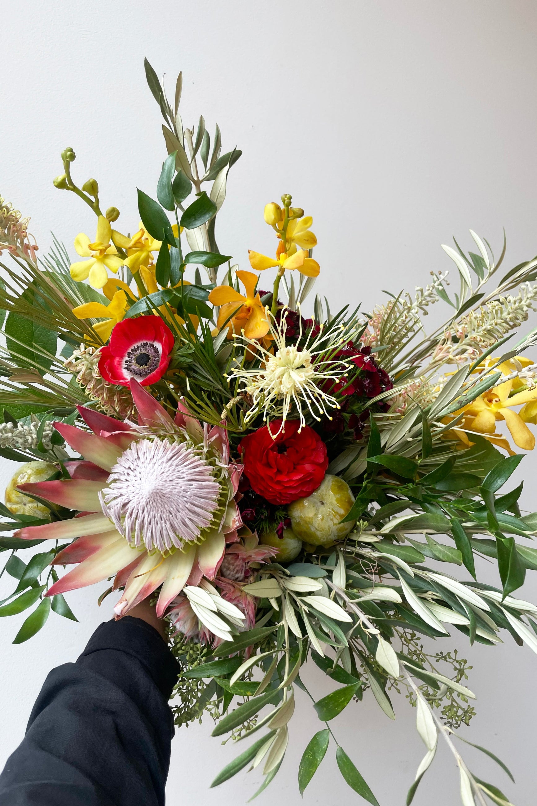 A hand holds an example of fresh Floral Arrangement Earth with white protea and yellow and red flowers from Sprout Home Floral in Chicago ©Sprout Home #size_$160