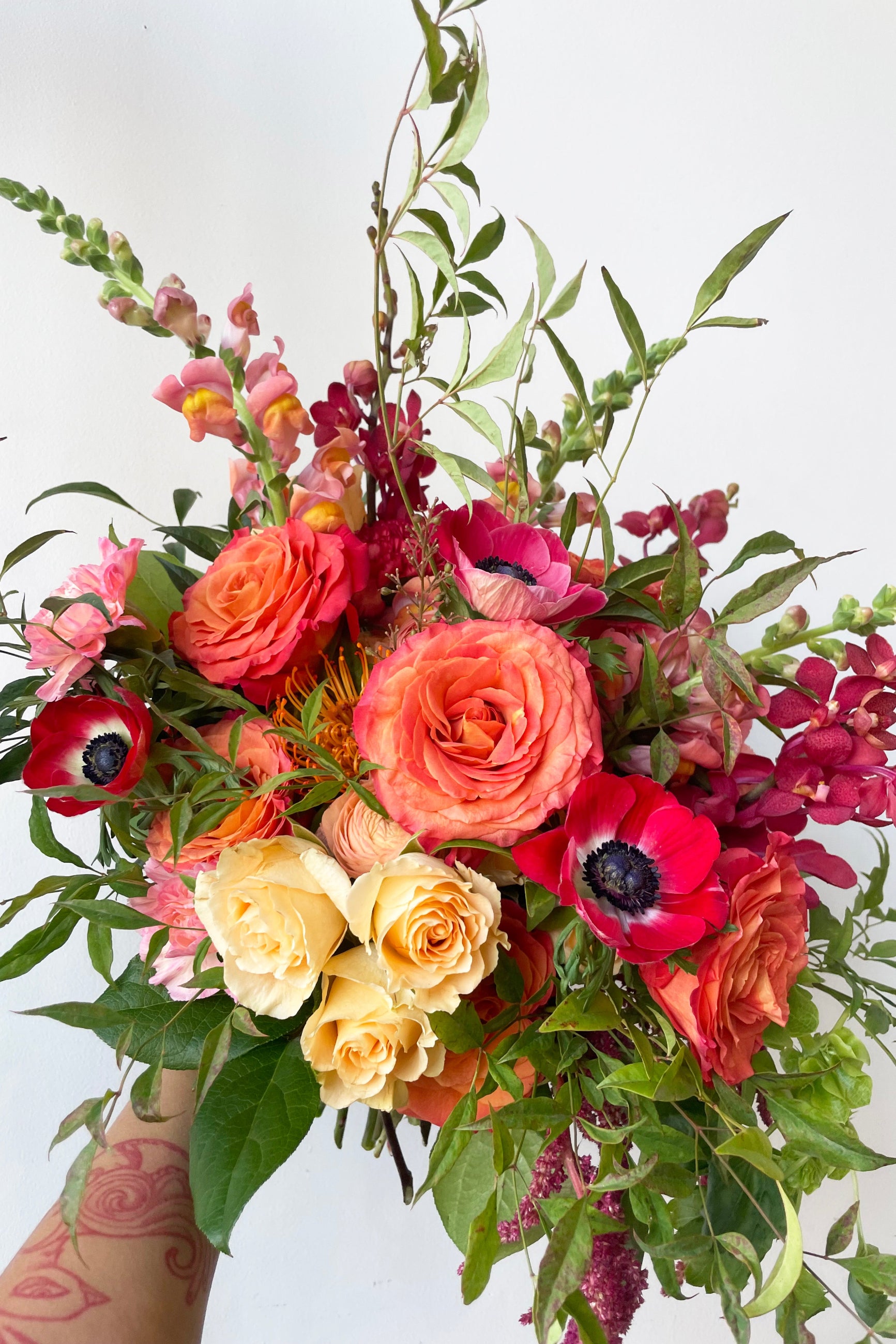 A hand holds an example of fresh Floral Arrangement Earth with huge coral roses and red anemone from Sprout Home Floral ©Sprout Home #size_$160