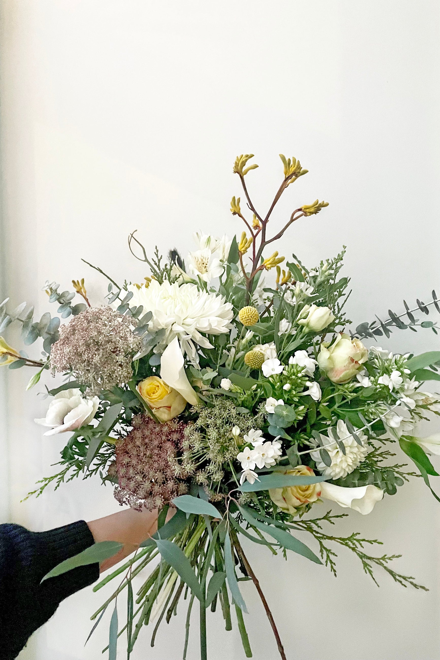 A hand holds an example of fresh Floral Arrangement Eggnog with pale blue foliage from Sprout Home Floral in Chicago ©Sprout Home #size_$160