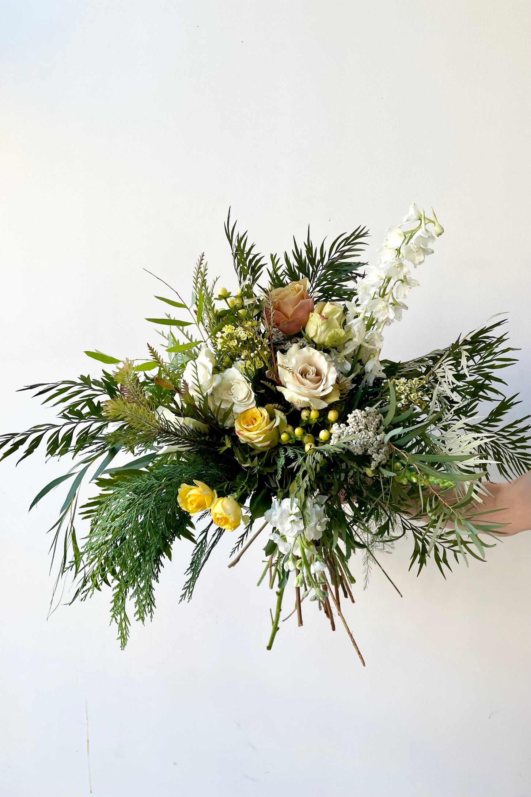 A hand holds fresh Floral Arrangement Eggnog for with white roses and evergreen from Sprout Home Floral in Chicago ©Sprout Home #size_$160