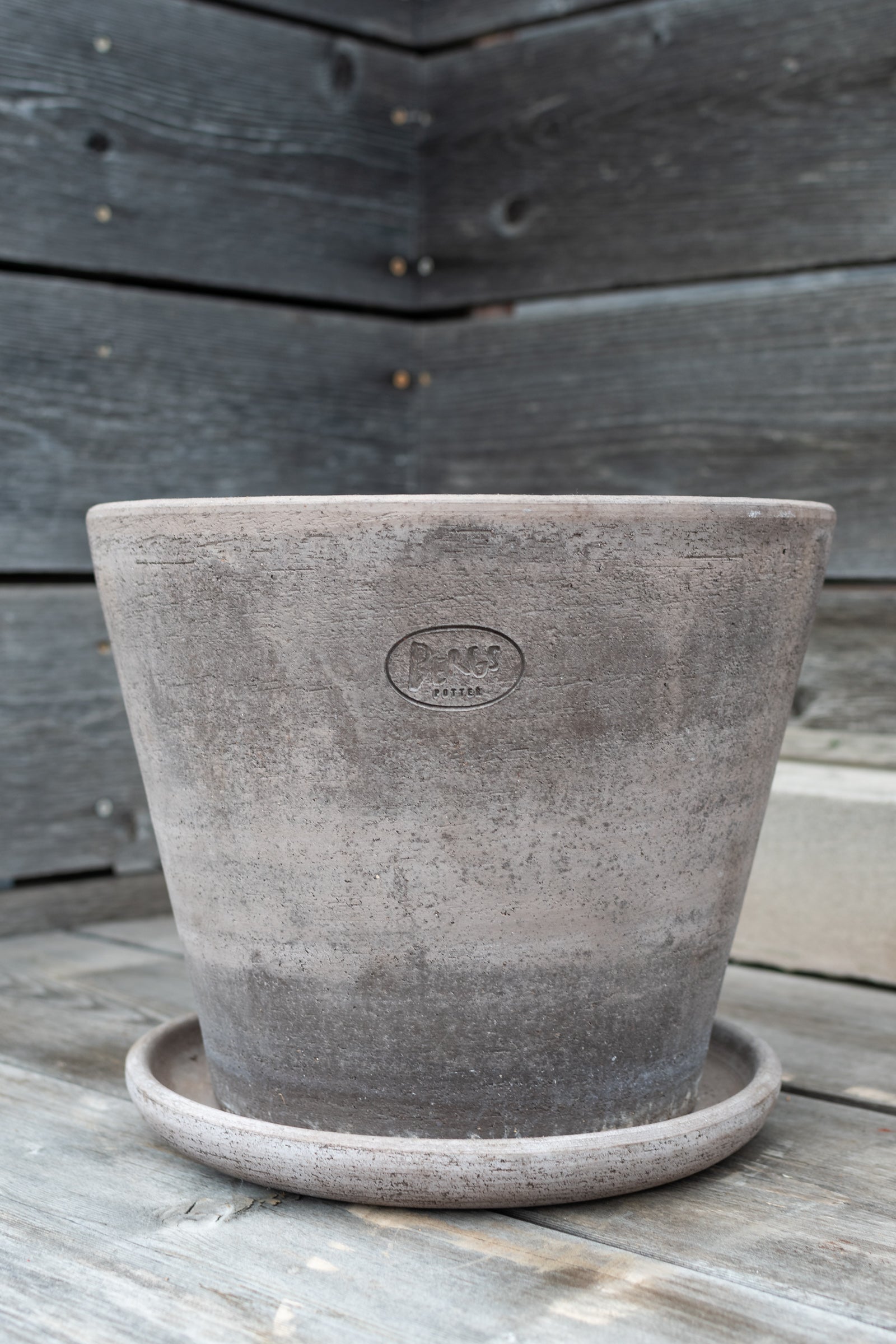 Julie pot by Bergs Potter in a gray color, empty and against a wood fence. ©Sprout Home