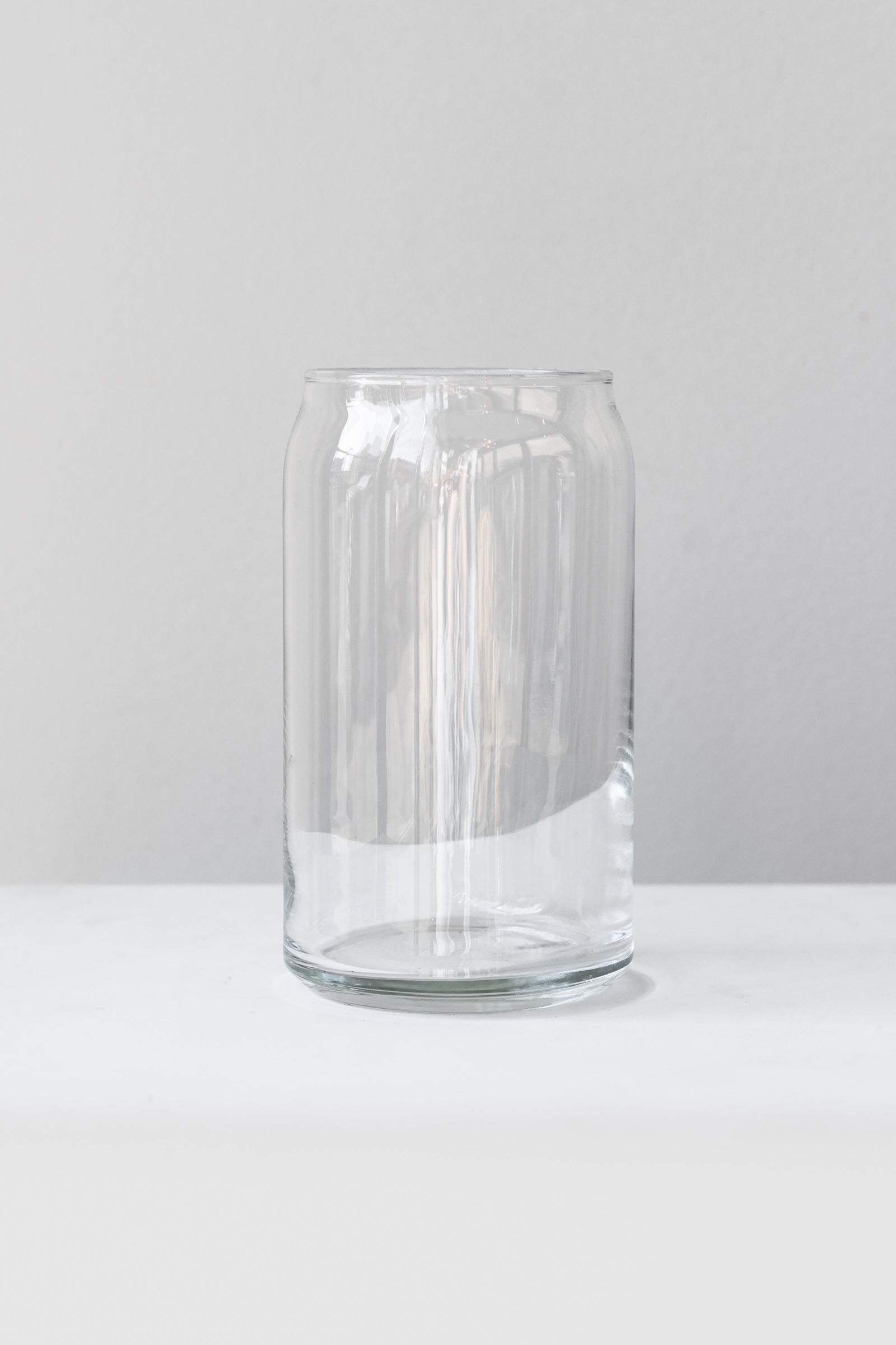 Clear glass jar sits on a white surface in a white room. The jar is shaped like a soda can. It is photographed straight on.