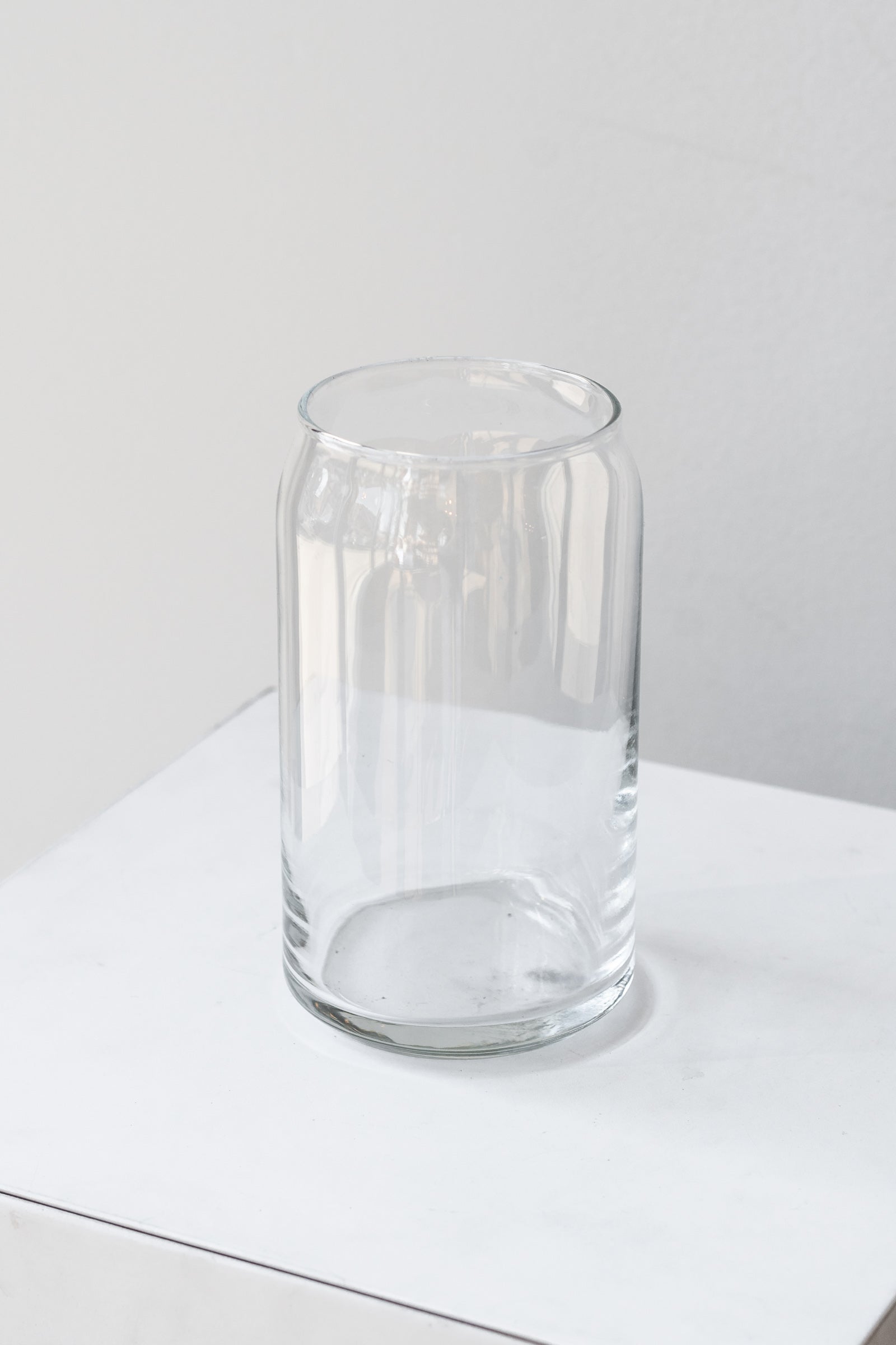 Clear glass jar sits on a white surface in a white room. The jar is shaped like a soda can. It is photographed closer and at an angle.