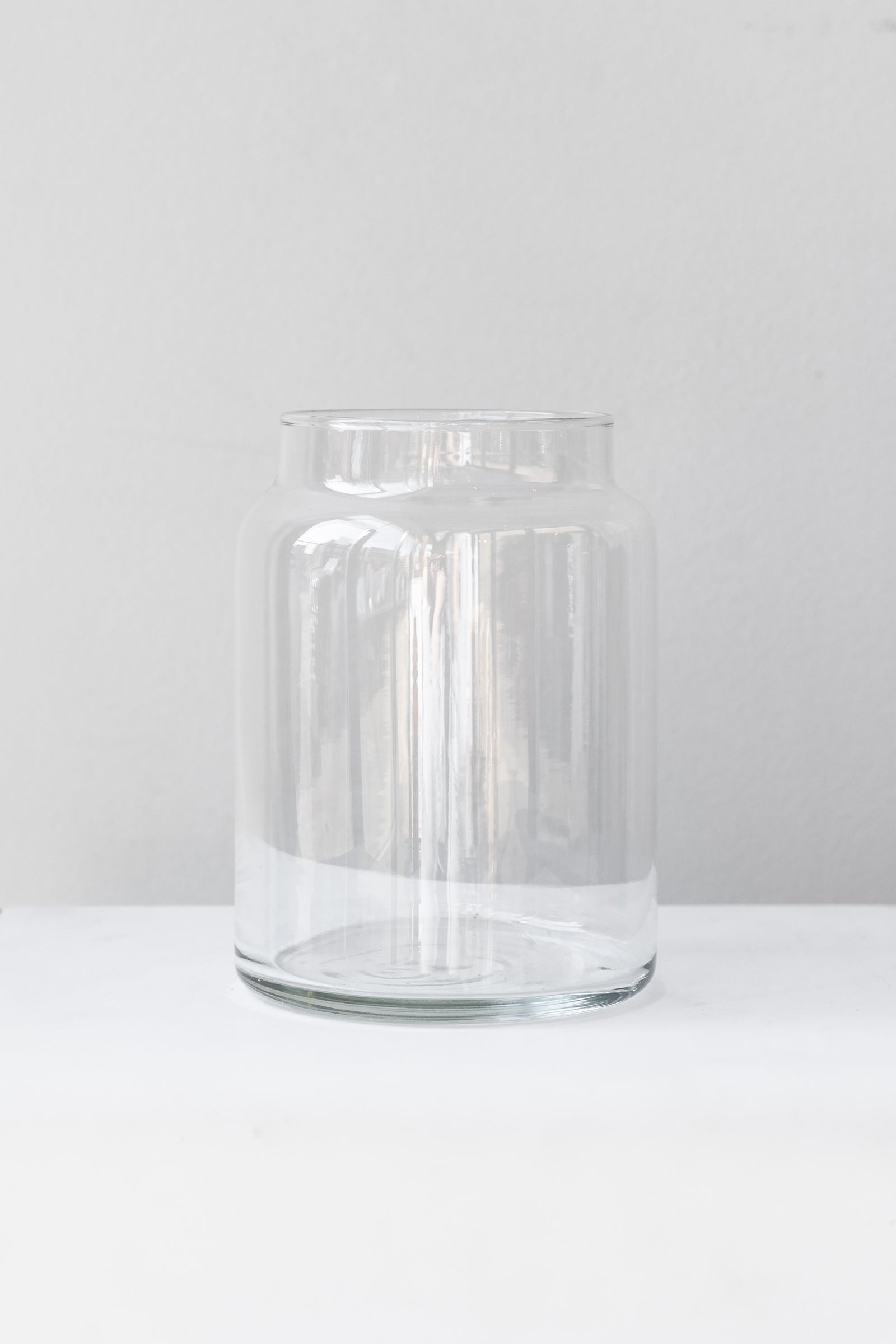 Clear glass jar sits on a white surface in a white room. It is photographed straight on.