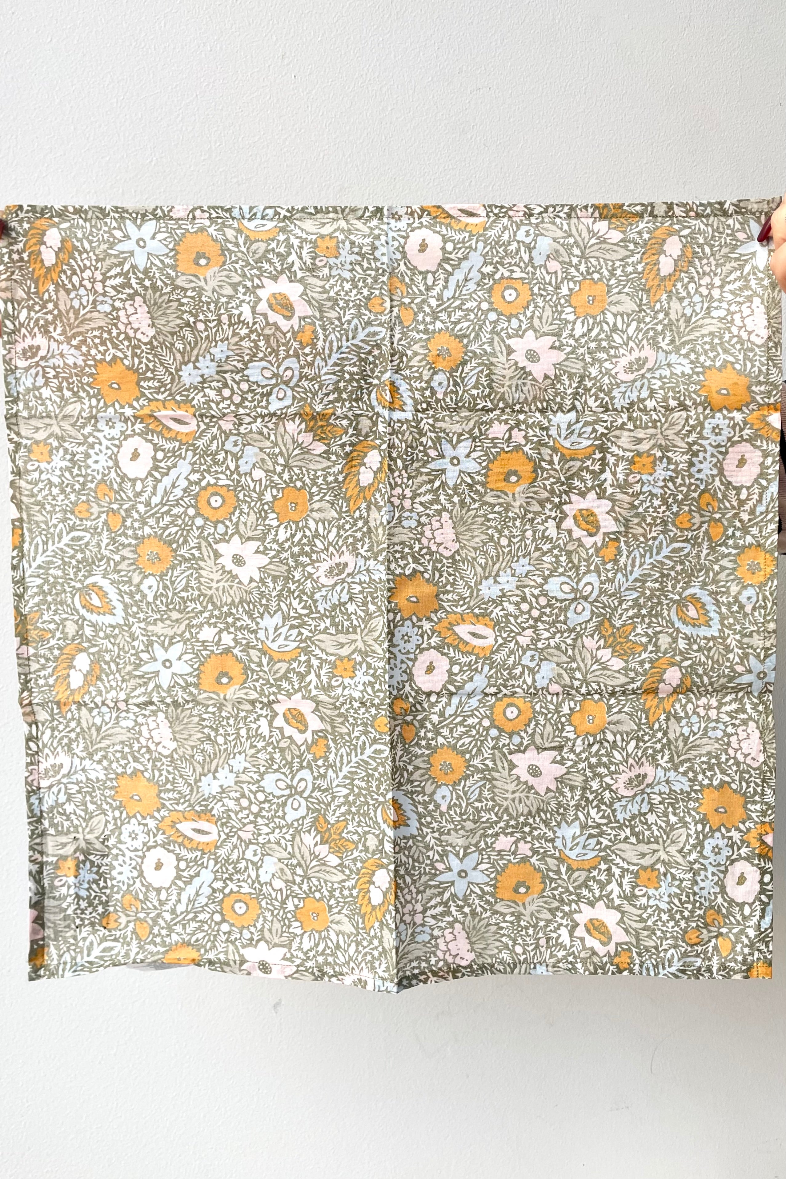 Hands hold up Cotton Napkins victoria orange, set of eight against a white backdrop