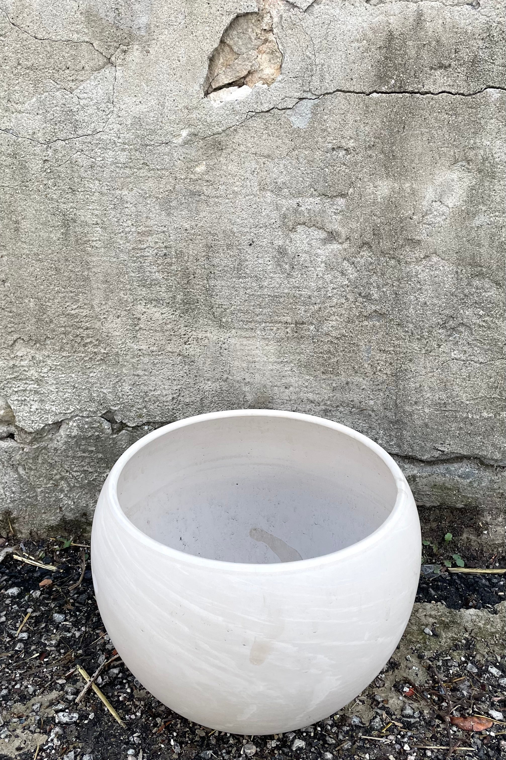A slightly overhead view of Luna Sphere Pot granite 10" against concrete backdrop