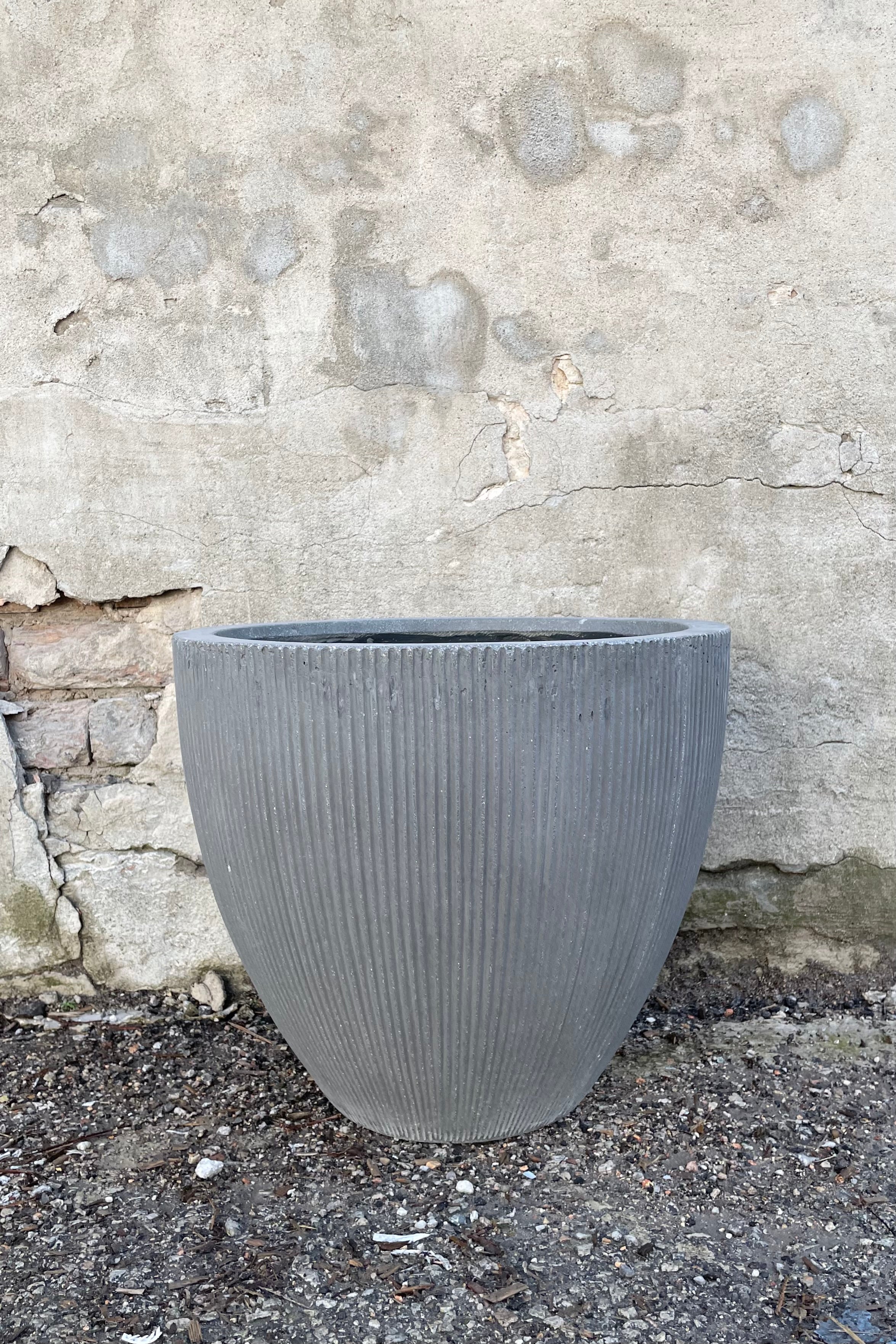 The dark grey extra small Jesslyn Pot with vertical ridges against a concrete wall at Sprout Home.