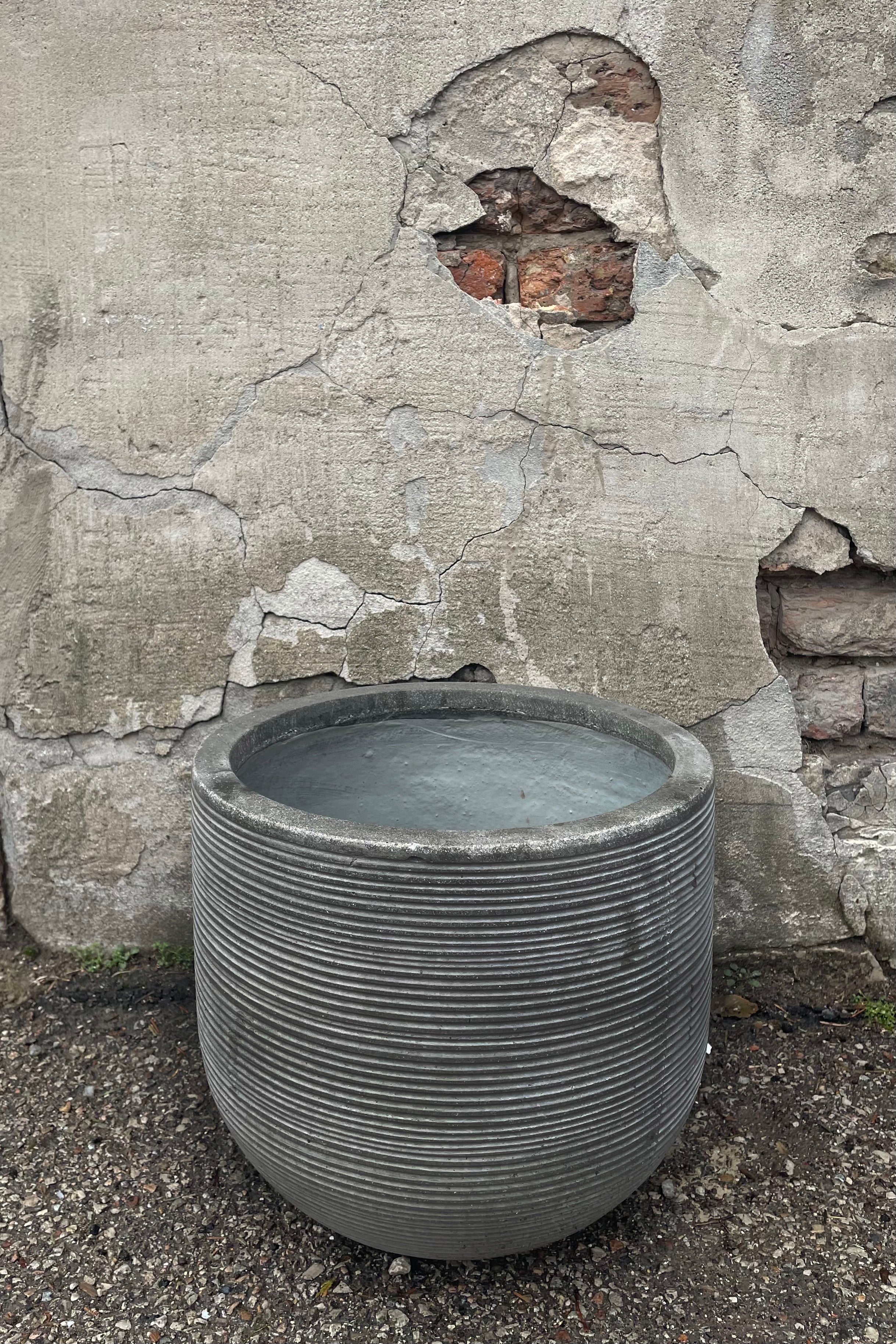 A slight overhead view of Cody Pot horizontal ridged dark grey medium against a concrete backdrop