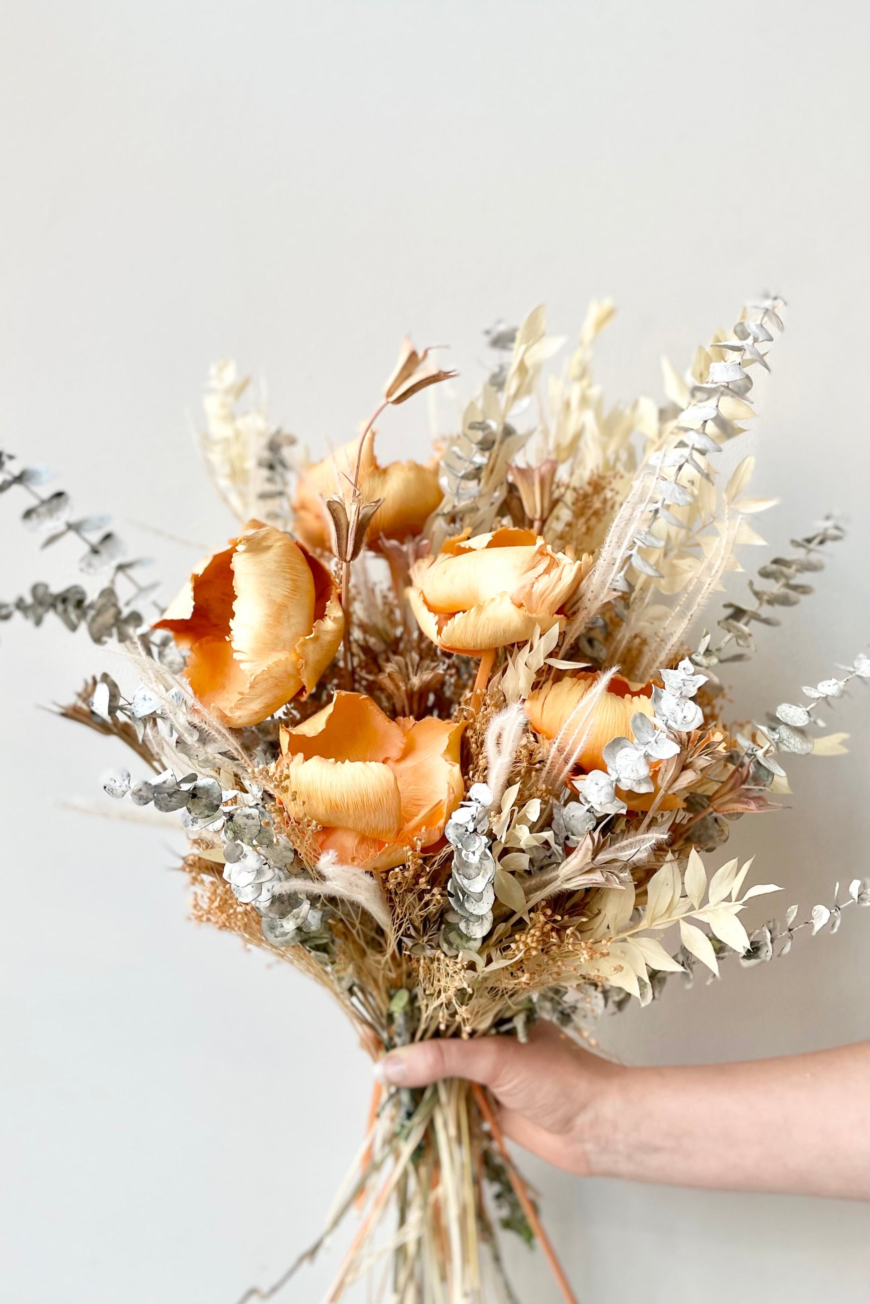 A hand holds the $125 option of Preserved Arrangement Creamsicle by Sprout Home against a white backdrop ©Sprout Home #size_$125