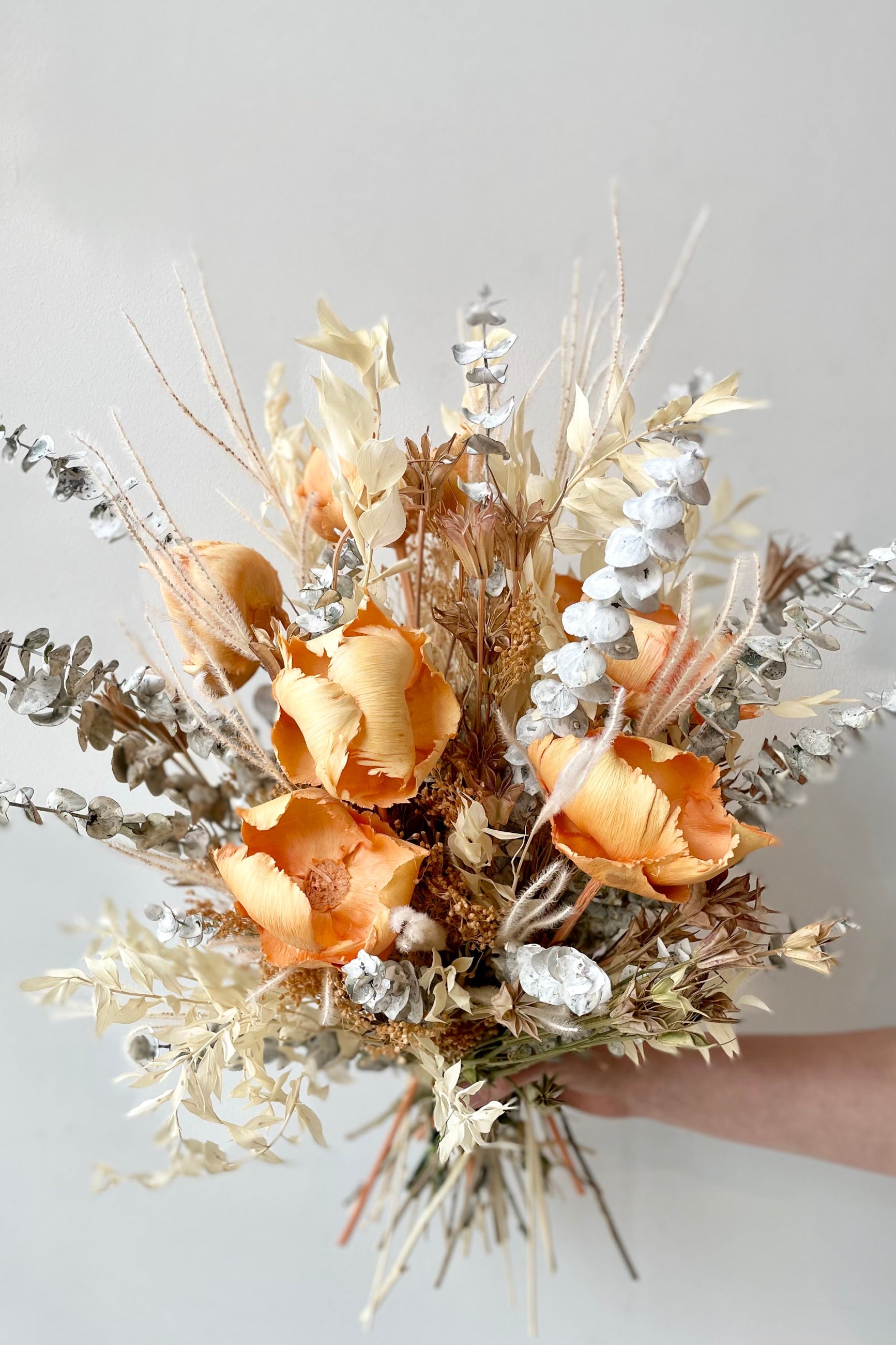 A hand holds the $160 option of Preserved Arrangement Creamsicle by Sprout Home against a white backdrop ©Sprout Home #size_$160