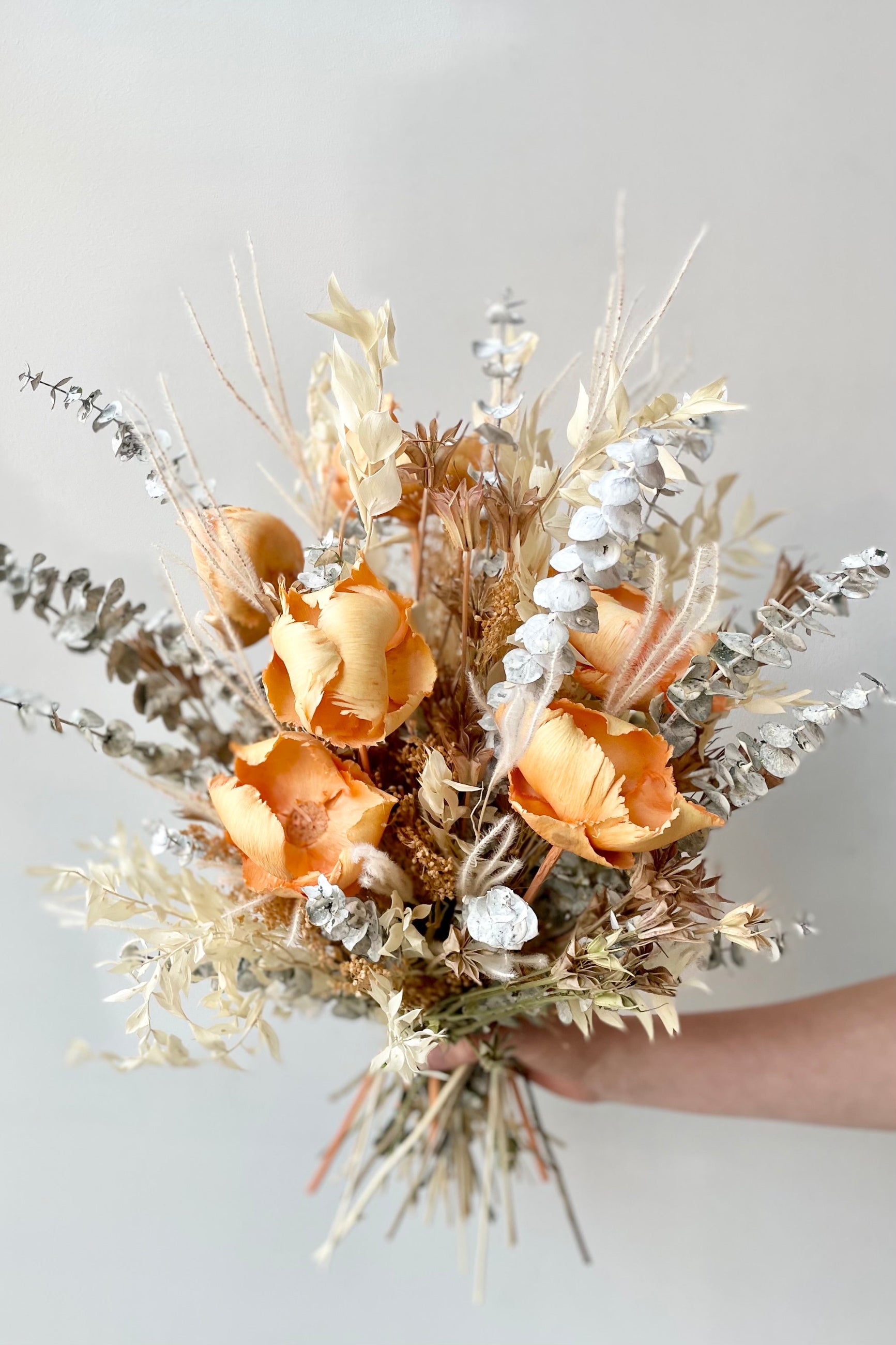 A hand holds the $160 option of Preserved Arrangement Creamsicle by Sprout Home against a white backdrop ©Sprout Home #size_$160
