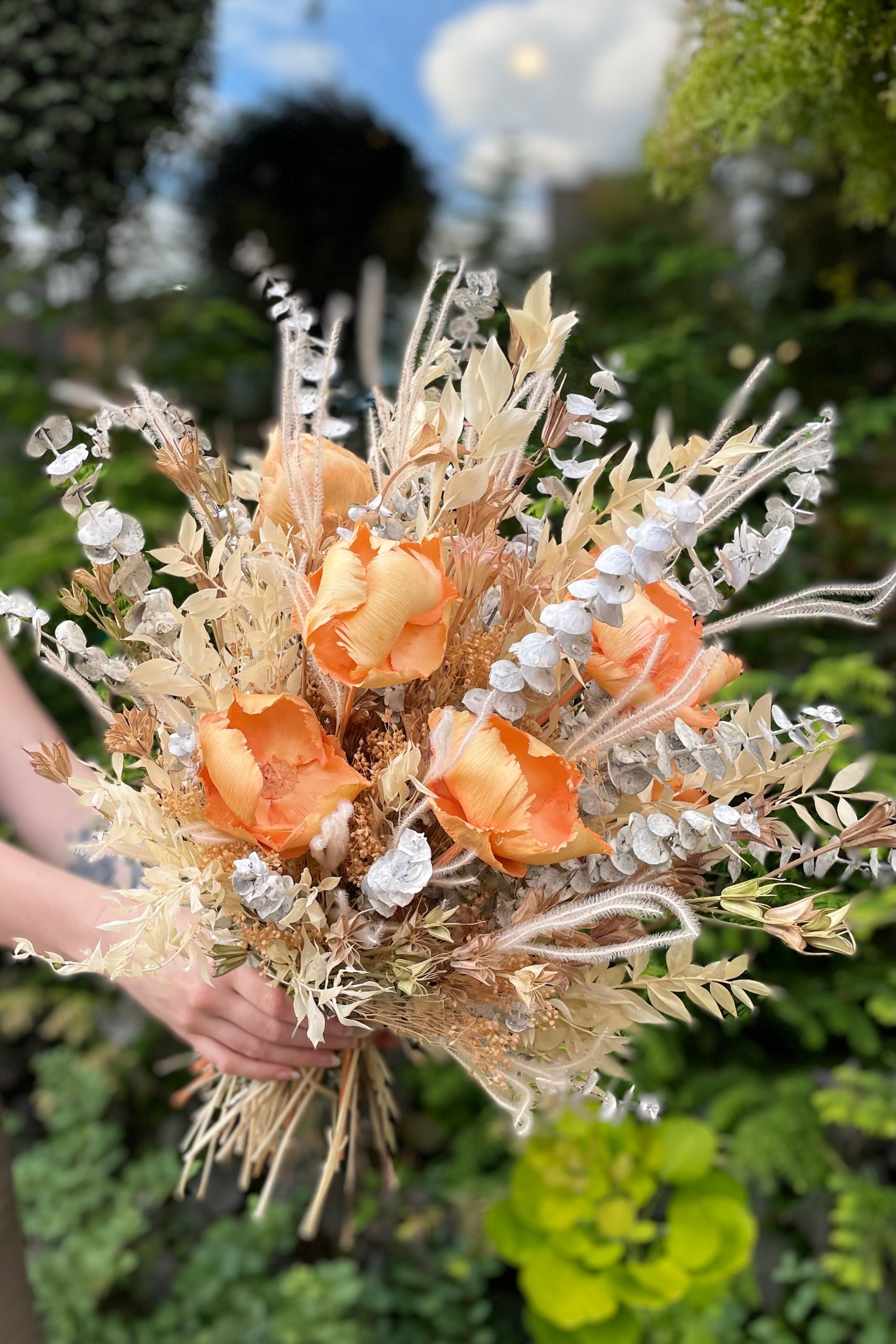 Two hands hold the $200 option for Preserved Arrangement Creamsicle against some greenery ©Sprout Home #size_$200