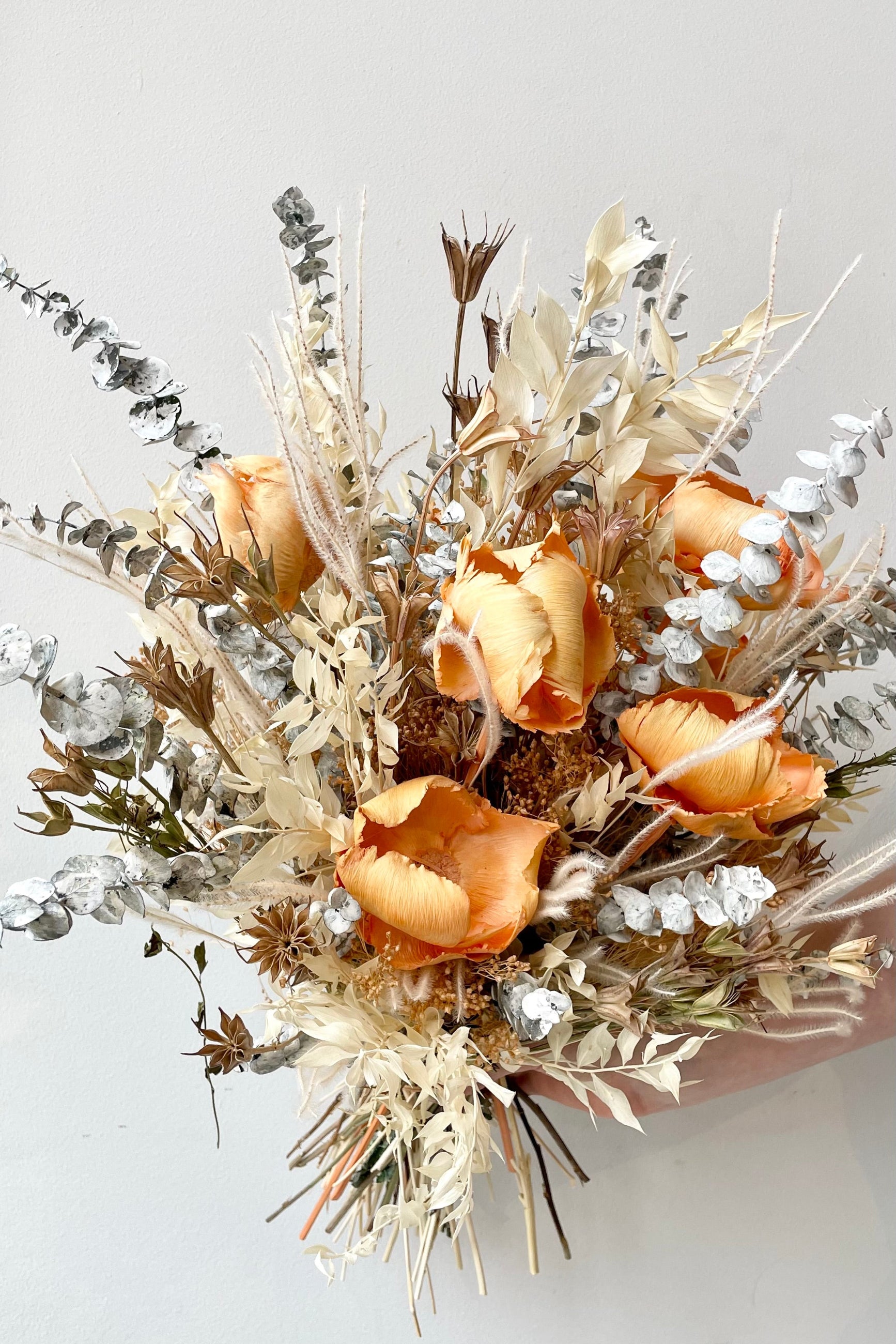 A hand holds the $200 option of Preserved Arrangement Creamsicle by Sprout Home against a white backdrop ©Sprout Home #size_$200