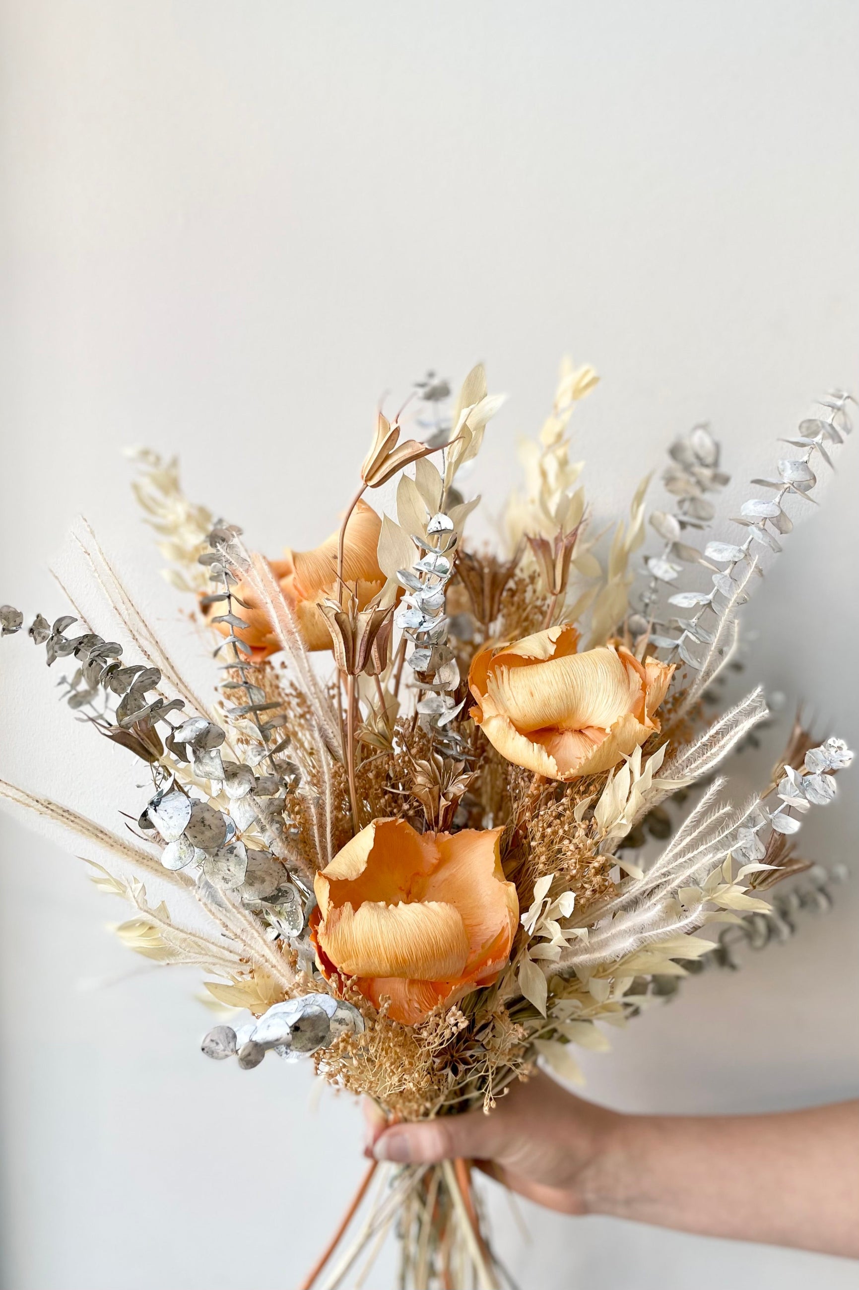 A hand holds the $85 option of Preserved Arrangement Creamsicle by Sprout Home against a white backdrop ©Sprout Home #size_$85