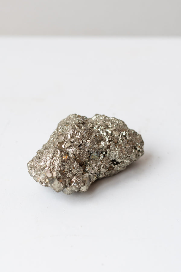 Pyrite (Fool's Gold) cluster on white surface in front of grey background