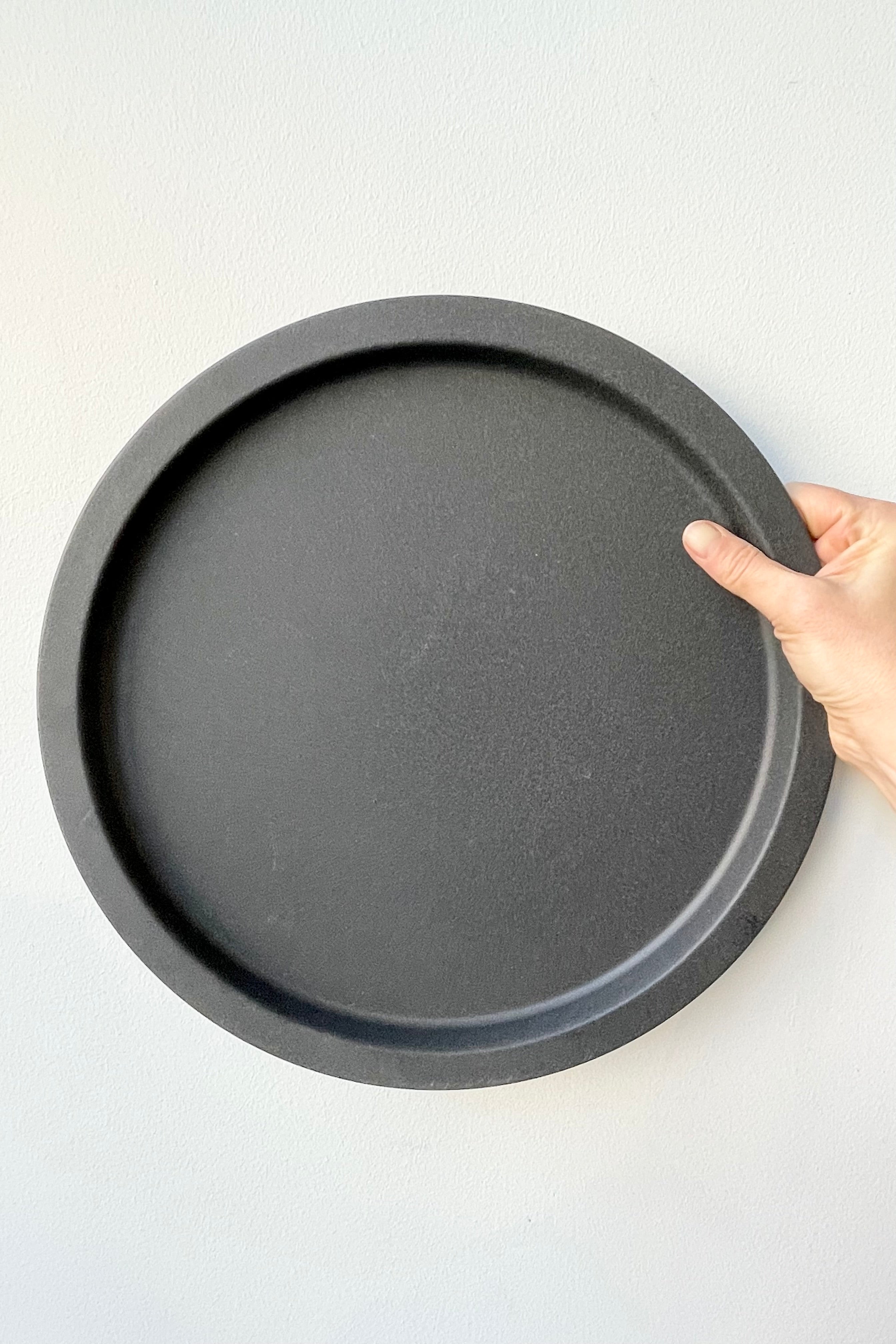 The grey speckled saucer being held against a white wall at Sprout Home