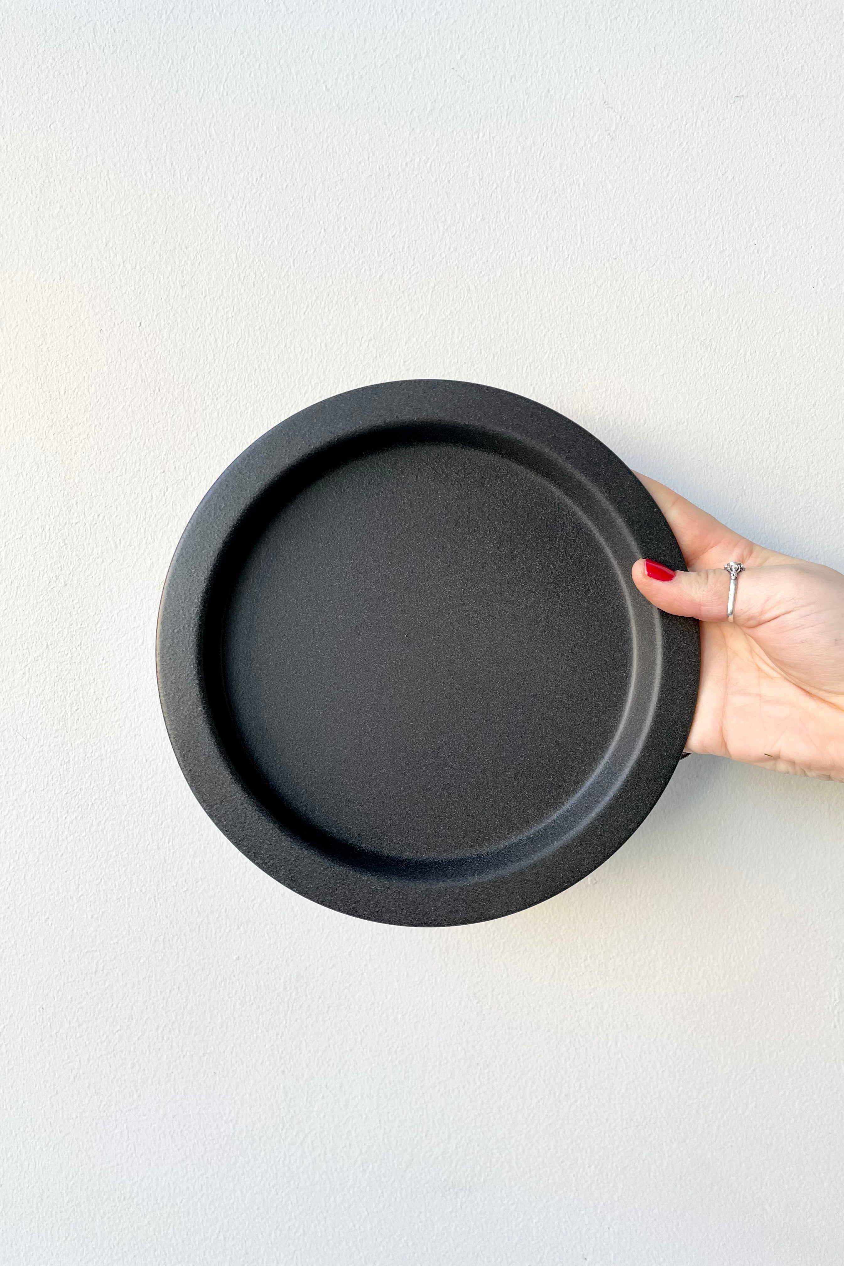 8" speckled grey saucer being held up against a white wall at Sprout Home.