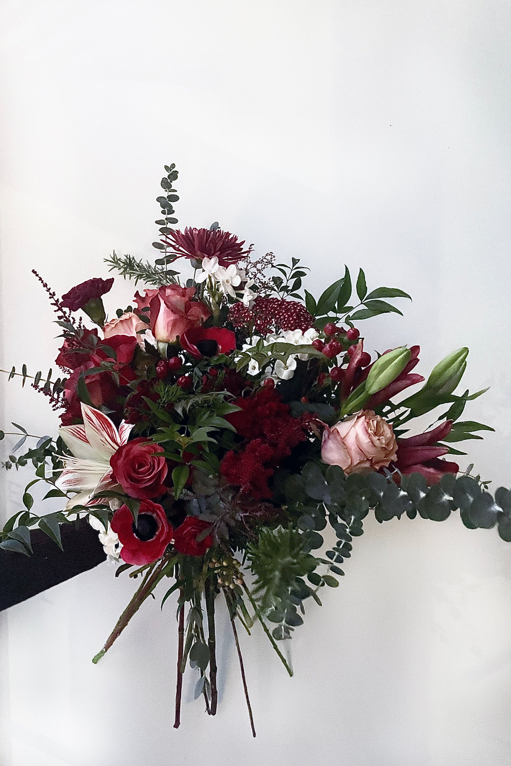 A hand holds an example of fresh Floral Arrangement Solstice with deep burgundy roses and dark foliage from Sprout Home Floral in Chicago ©Sprout Home #size_$130