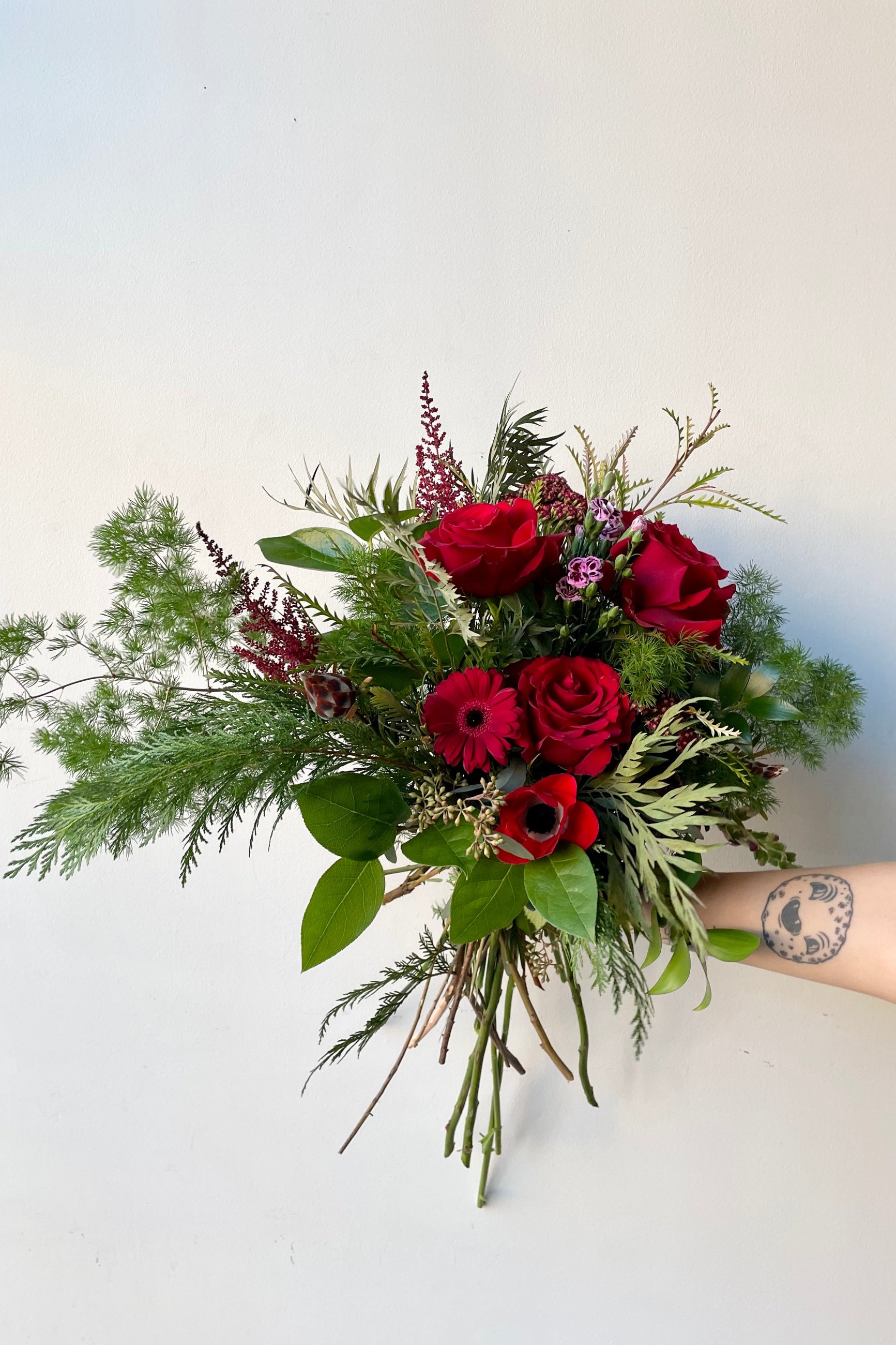 A hand holds an example of fresh Floral Arrangement Solstice with red roses and daisy from Sprout Home Floral in Chicago ©Sprout Home #size_$130