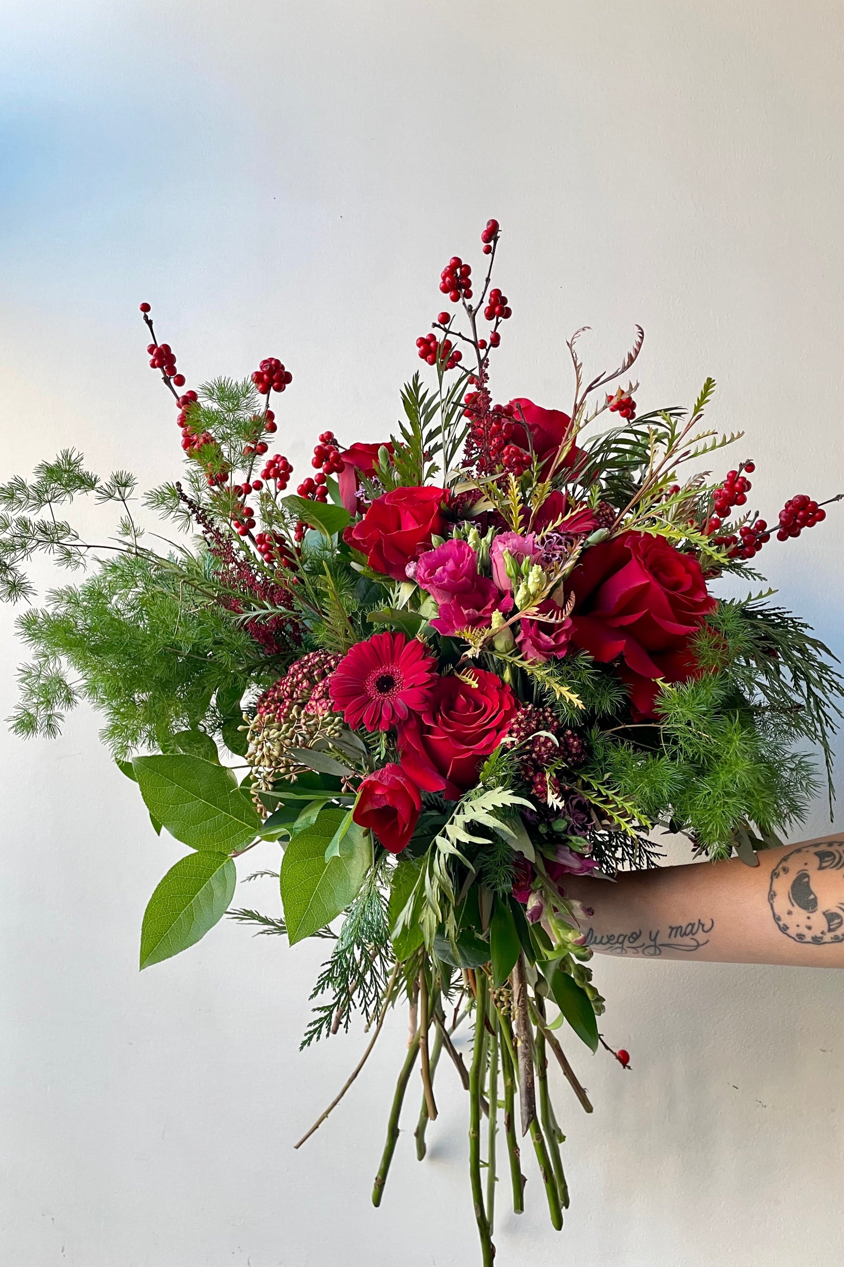 A hand holds an example of fresh Floral Arrangement Solstice large and in charge with shades of red from Sprout Home Floral in Chicago ©Sprout Home #size_$200