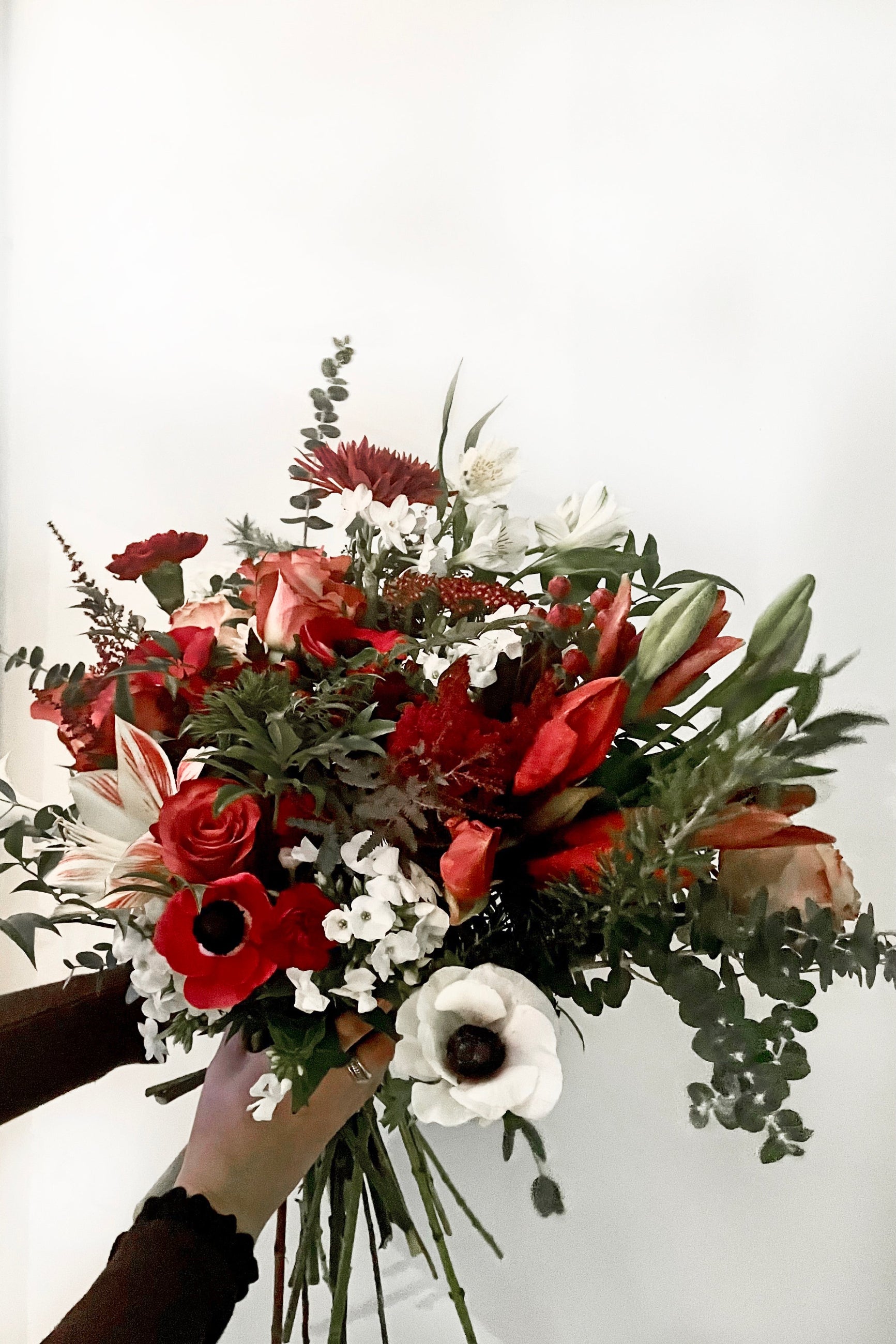 A hand holds an example of fresh Floral Arrangement Solstice with sexy foliage and maroon and red flowers from Sprout Home Floral in Chicago ©Sprout Home #size_$160