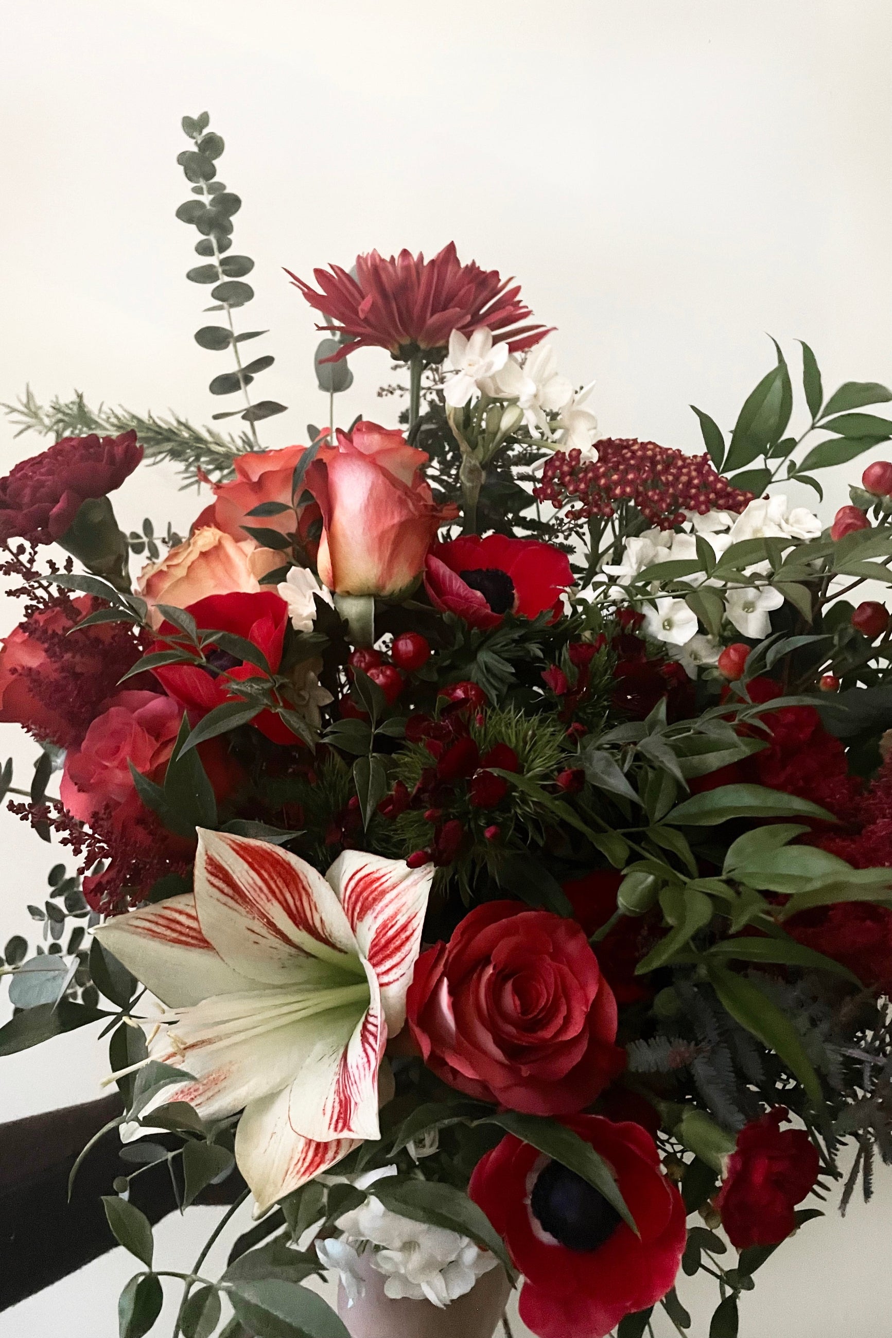 A hand holds an example of fresh Floral Arrangement Solstice with amaryllis and various red flowers from Sprout Home Floral in Chicago #size_130