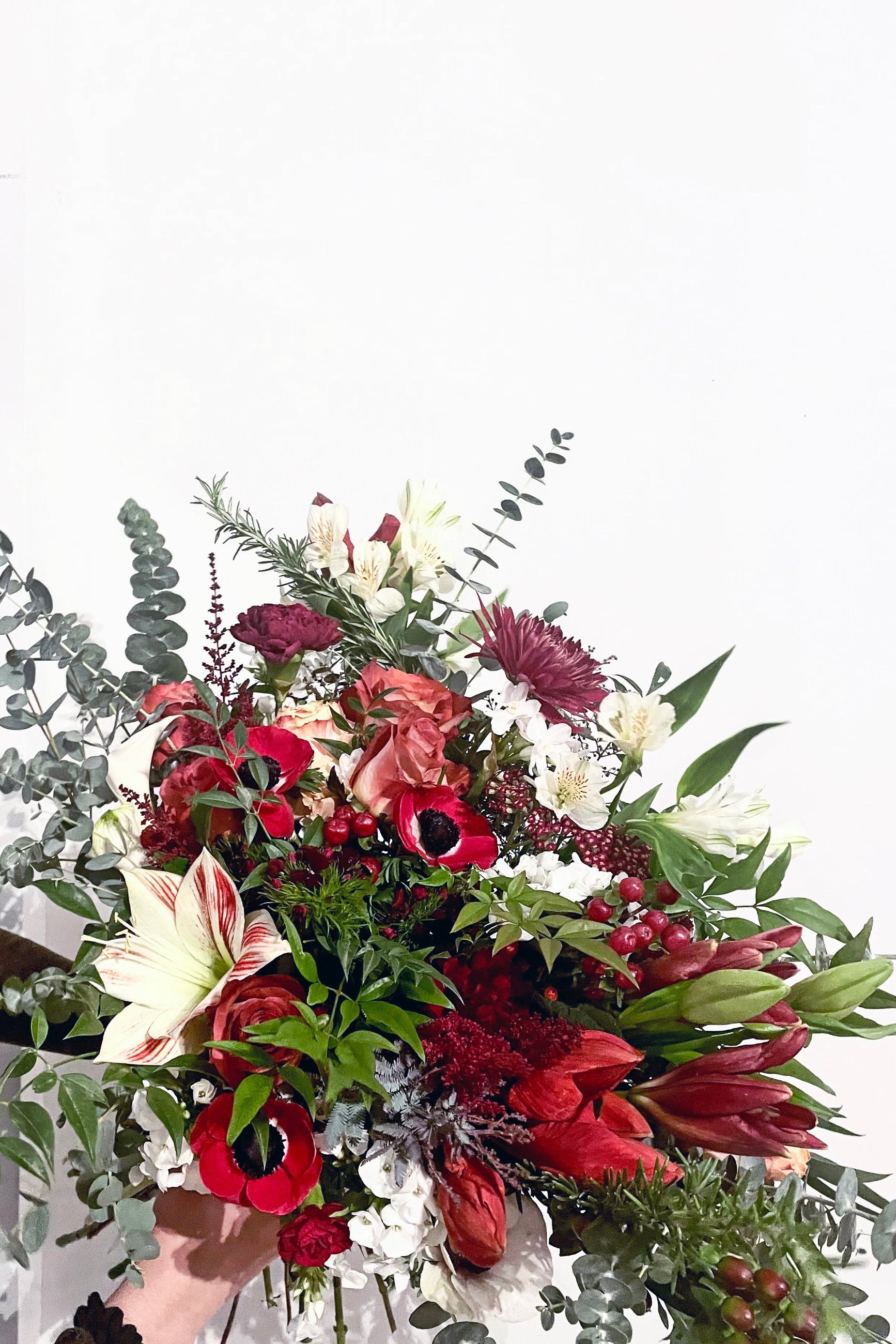 A hand holds an example of fresh Floral Arrangement Solstice with winter foliage and Res from Sprout Home Floral in Chicago ©Sprout Home #size_$200