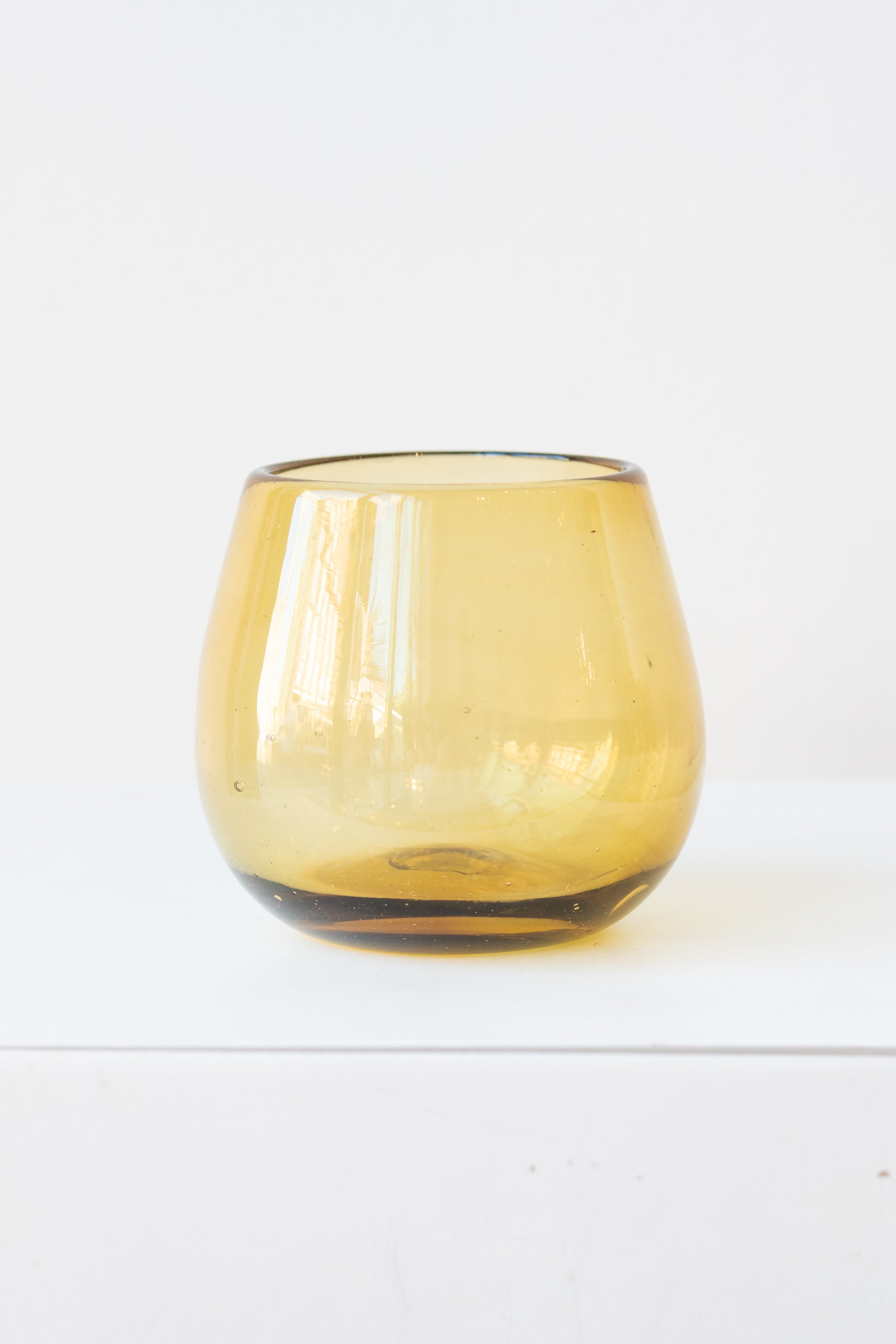 Stemless amber colored wine glass on a white surface in a white room