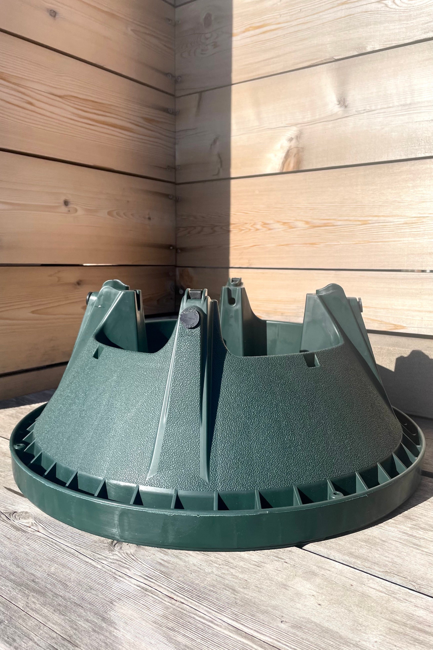 A green plastic Christmas tree stand designed to hold trees up to 10 feet in height, with visible bolts and reservoir for water. ©Sprout Home